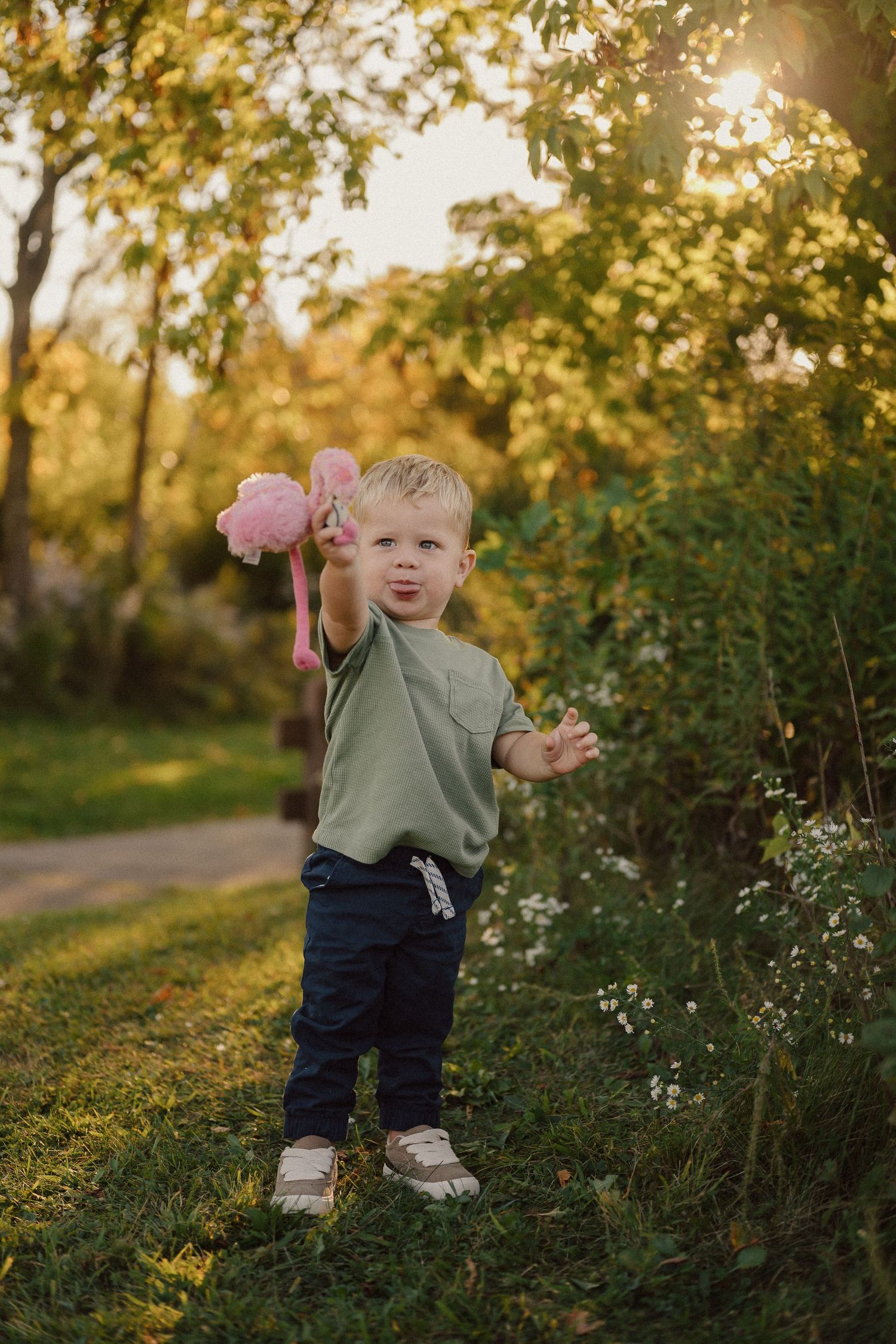 A toddler plays with pink flowers in a garden during golden hour sunlight.