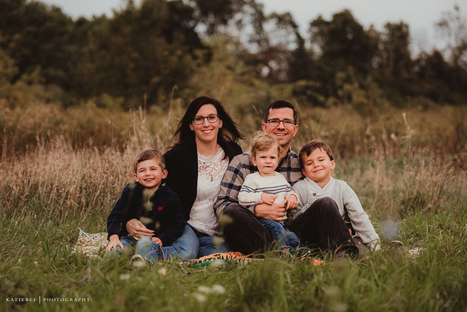 Family relaxing together on grass in a sunlit meadow during golden hour.
