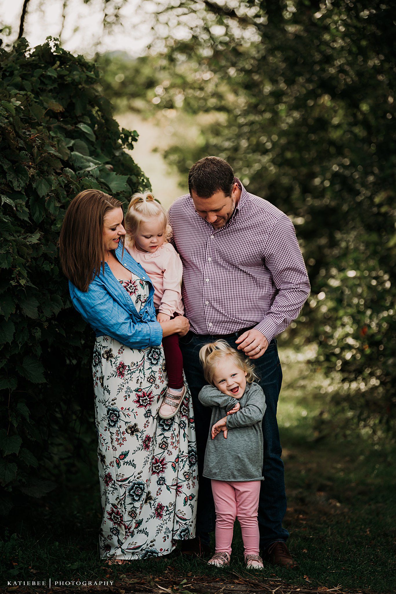 A tender family portrait taken outdoors against a backdrop of lush greenery.