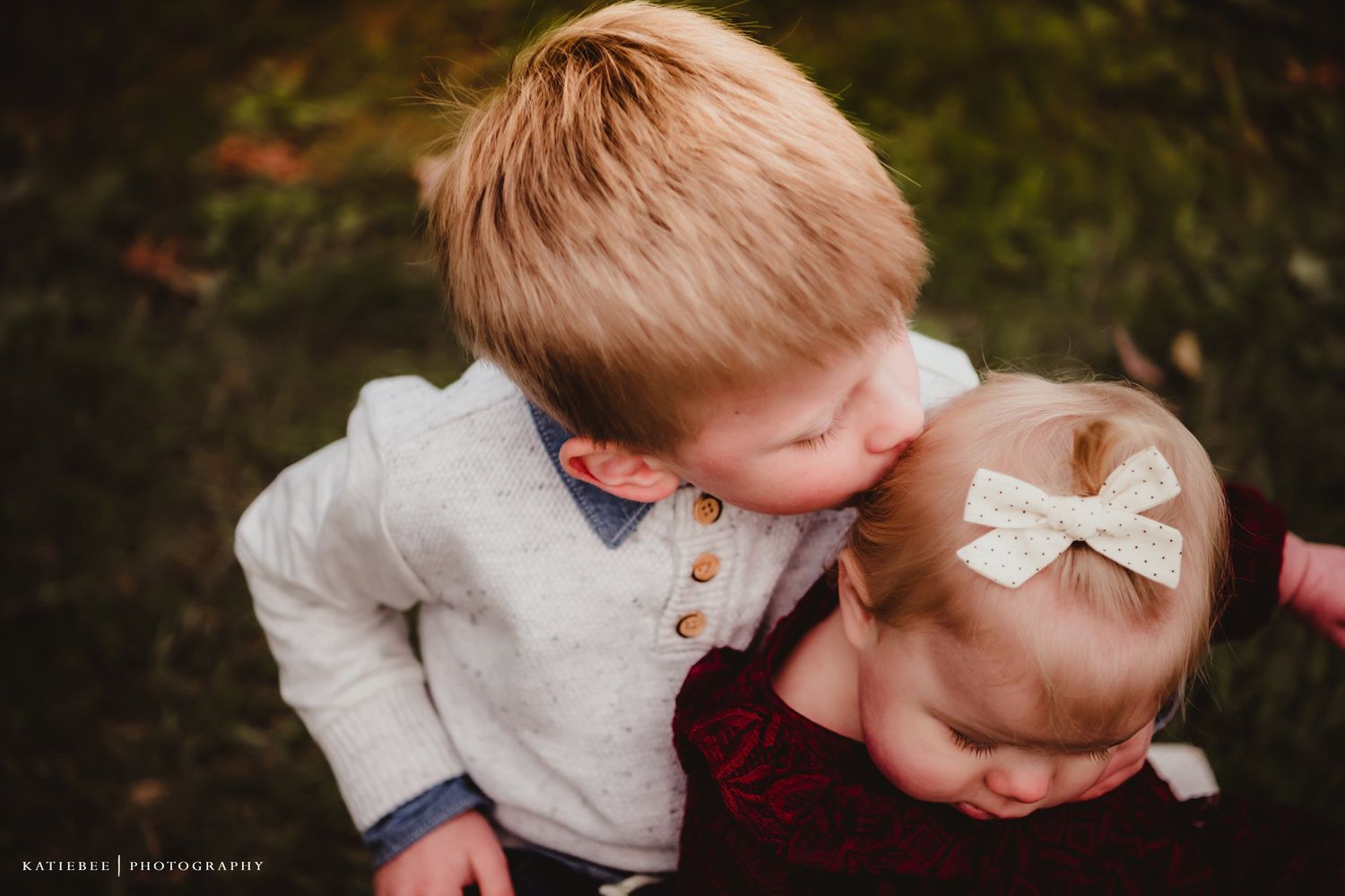 Two young children sharing a tender moment while wearing coordinated winter outfits in an outdoor setting.