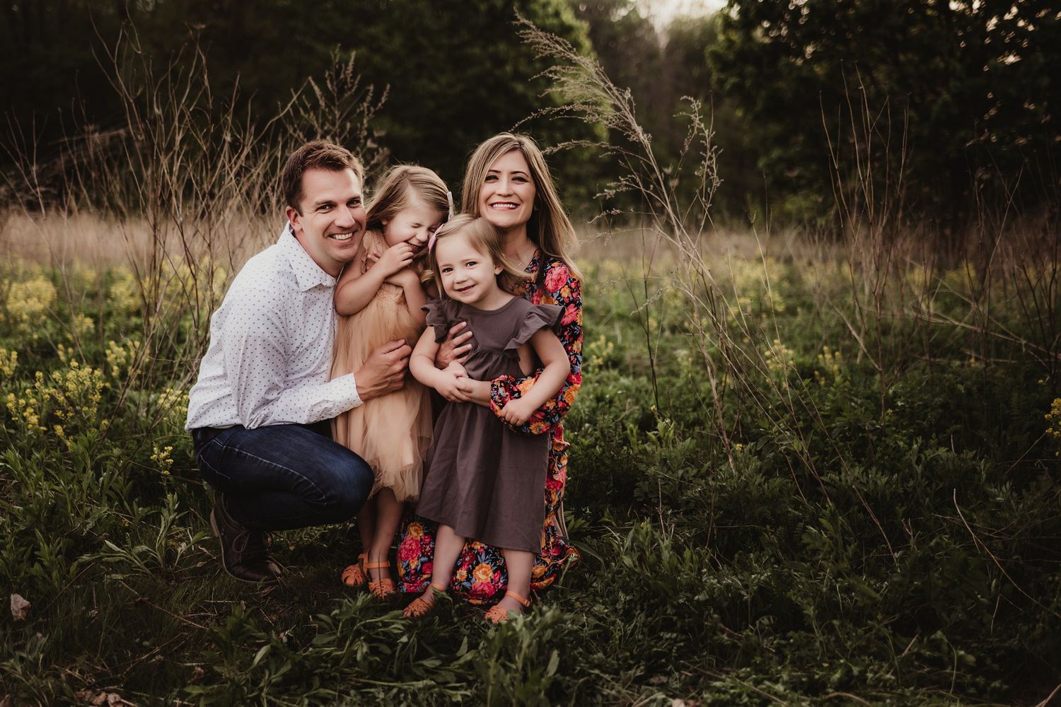 Family portrait in rustic outdoor setting with golden hour lighting and wild flowers.