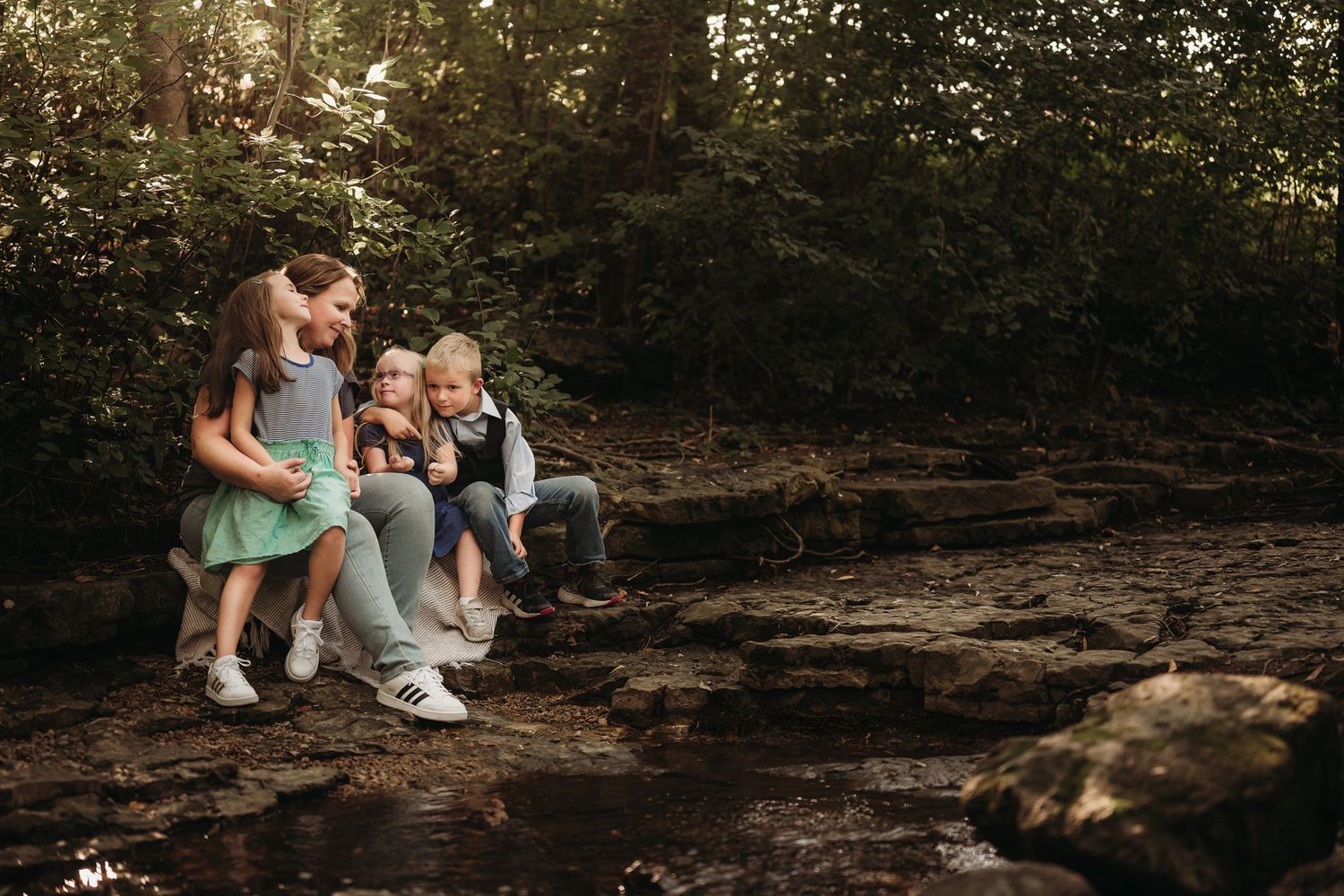 Family members sit together on rocks in a wooded outdoor setting.