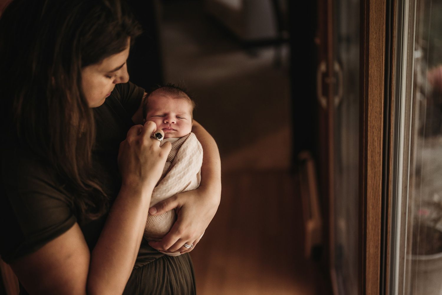 Gentle indoor portrait of newborn swaddled in soft blanket by window light.