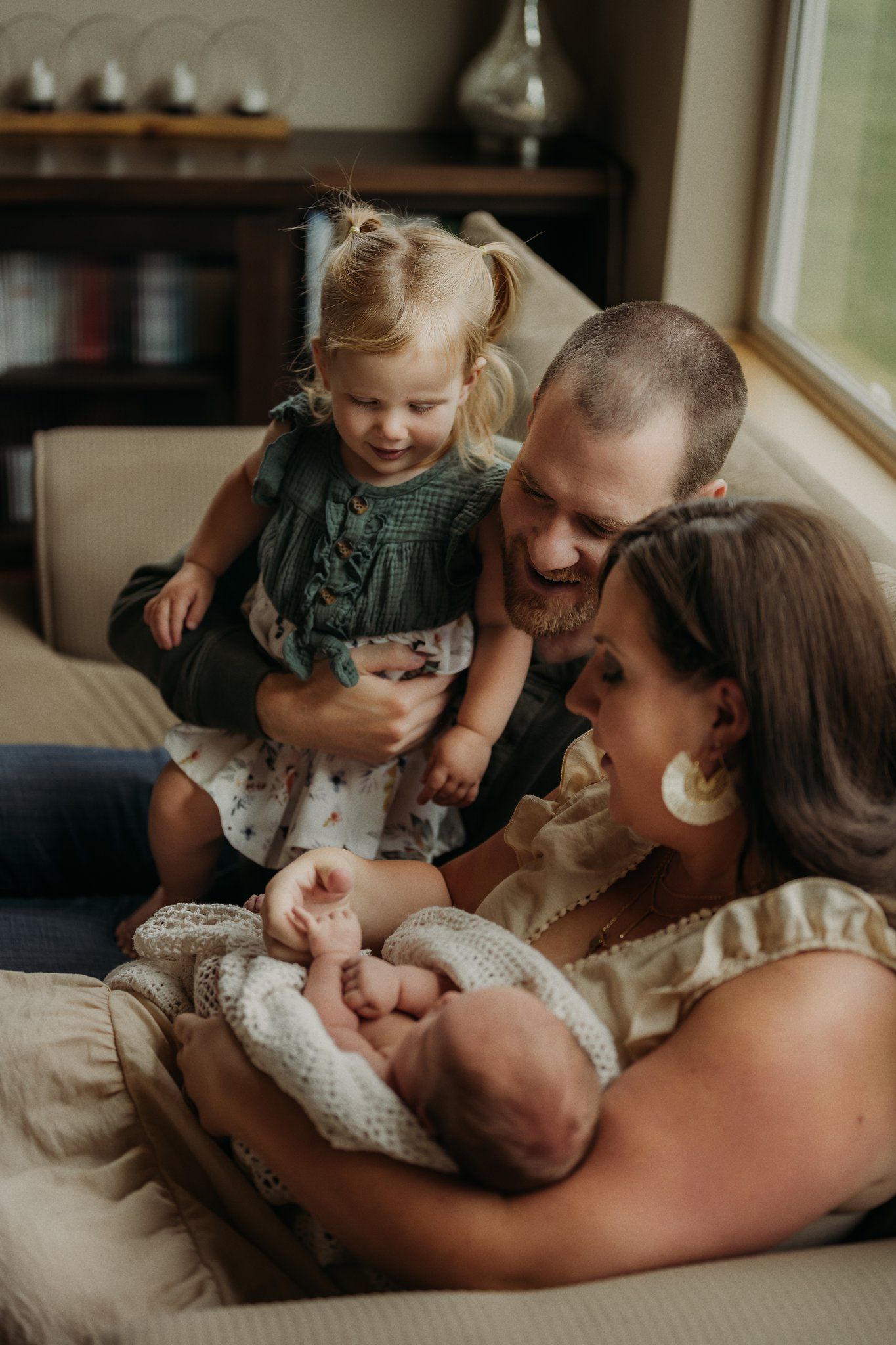 A tender family moment on a couch as they gather around a newborn wrapped in a blanket.