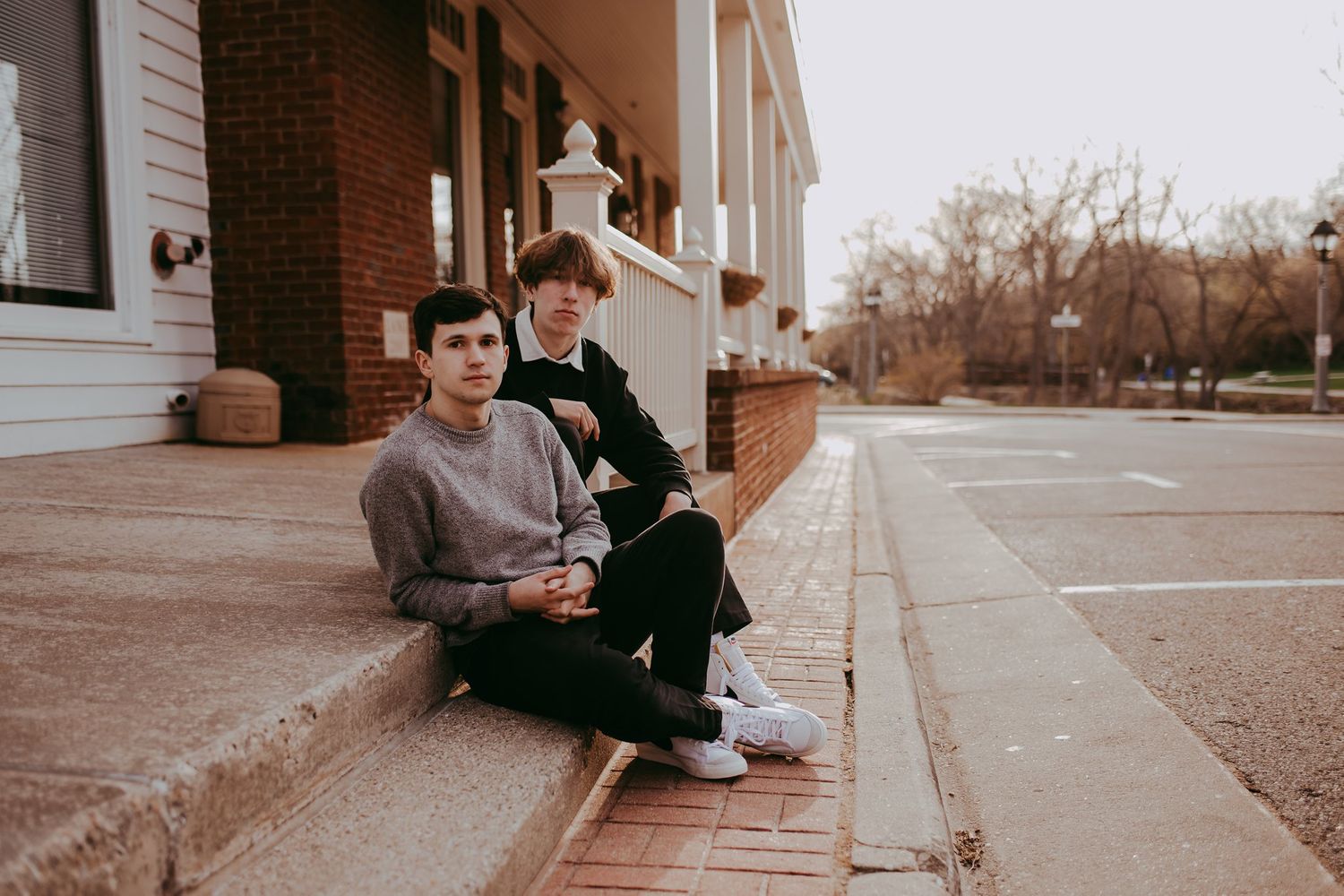 Two people sit casually on steps outside a brick building with white columns.