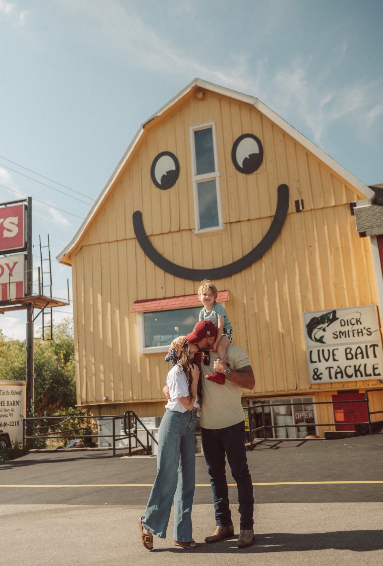 A couple posing in front of a yellow building with a large smiley face painted on its facade.
