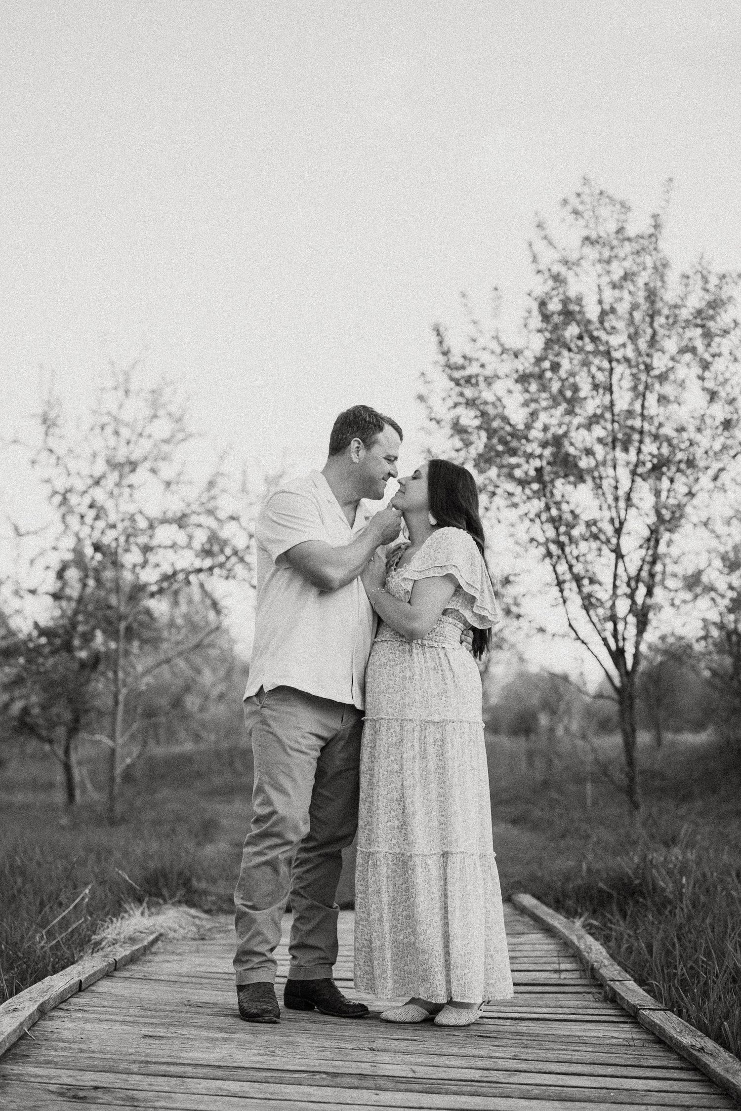A couple shares a tender romantic moment on a wooden boardwalk in a black and white photo.