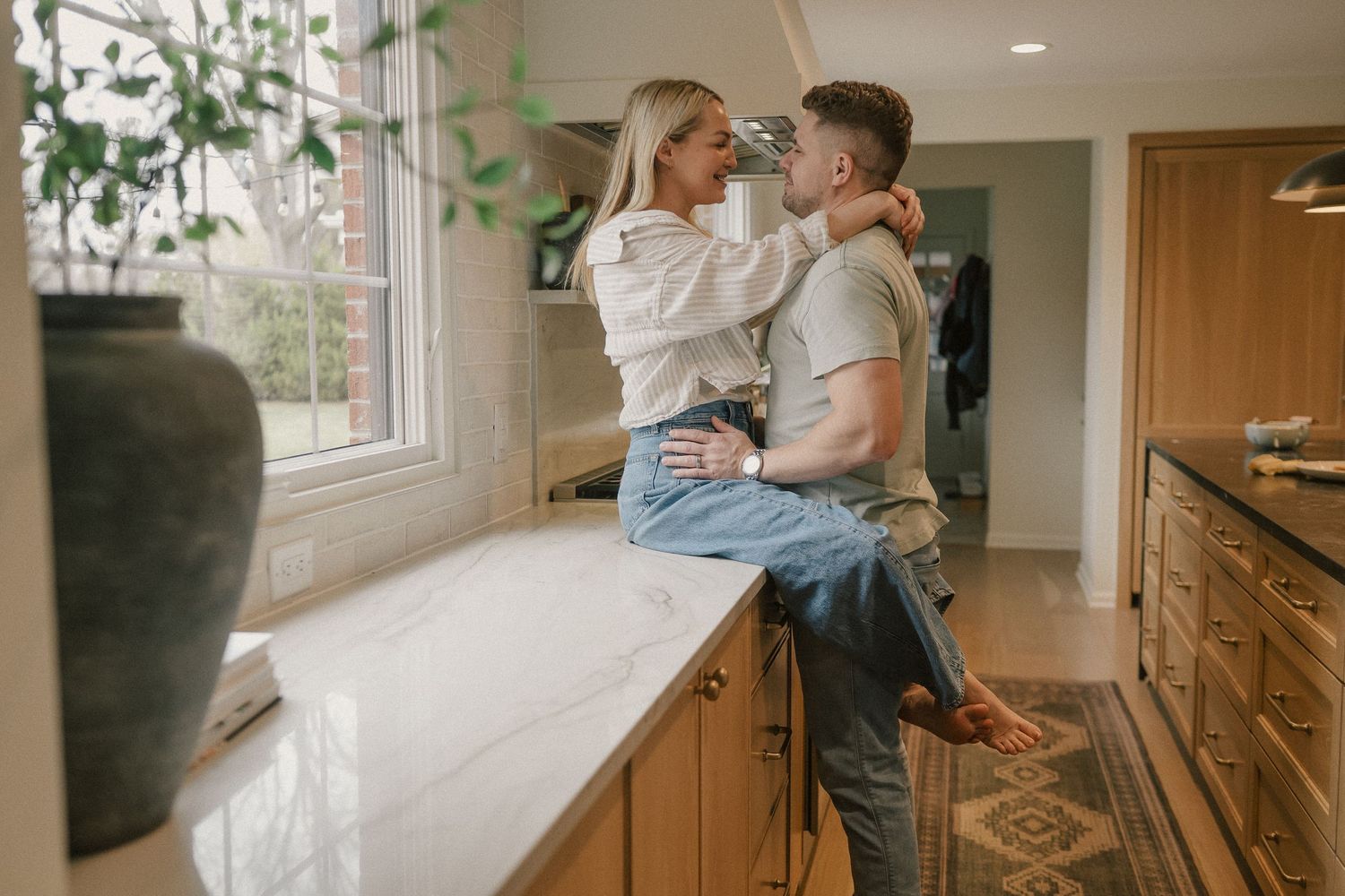 A couple shares a romantic moment as the woman sits on a marble kitchen countertop.