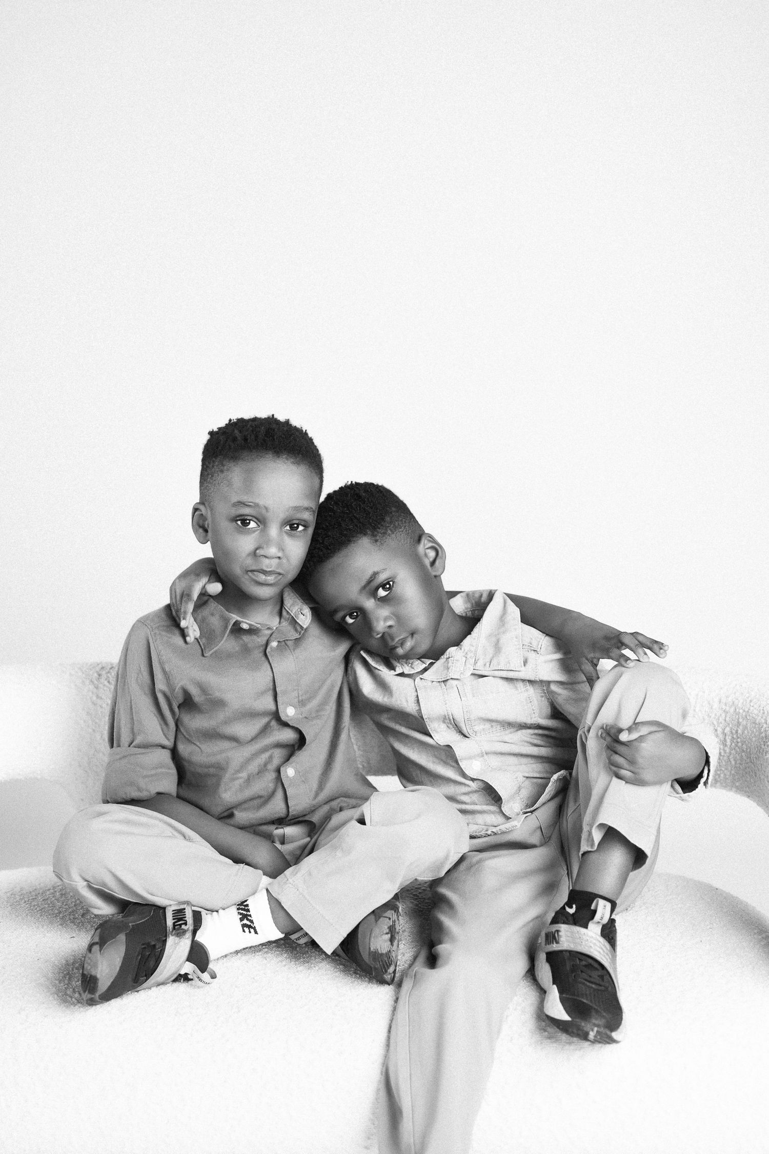 Two children relax and lean on each other in a casual black and white portrait.