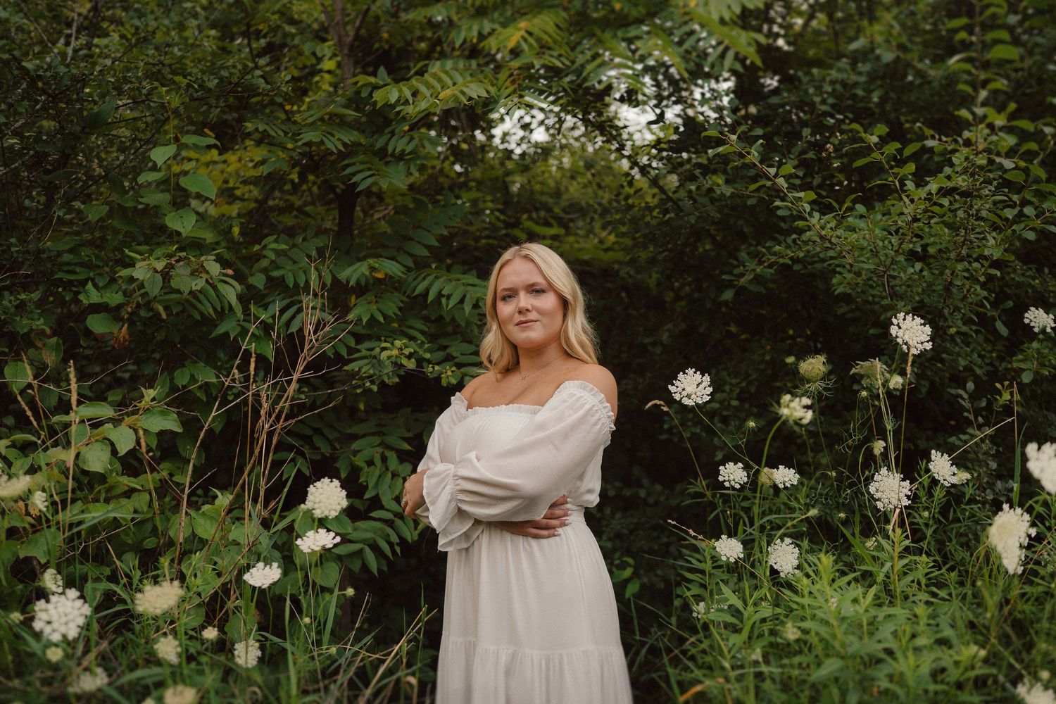 Person in white dress posing near flowering white roses in a garden.