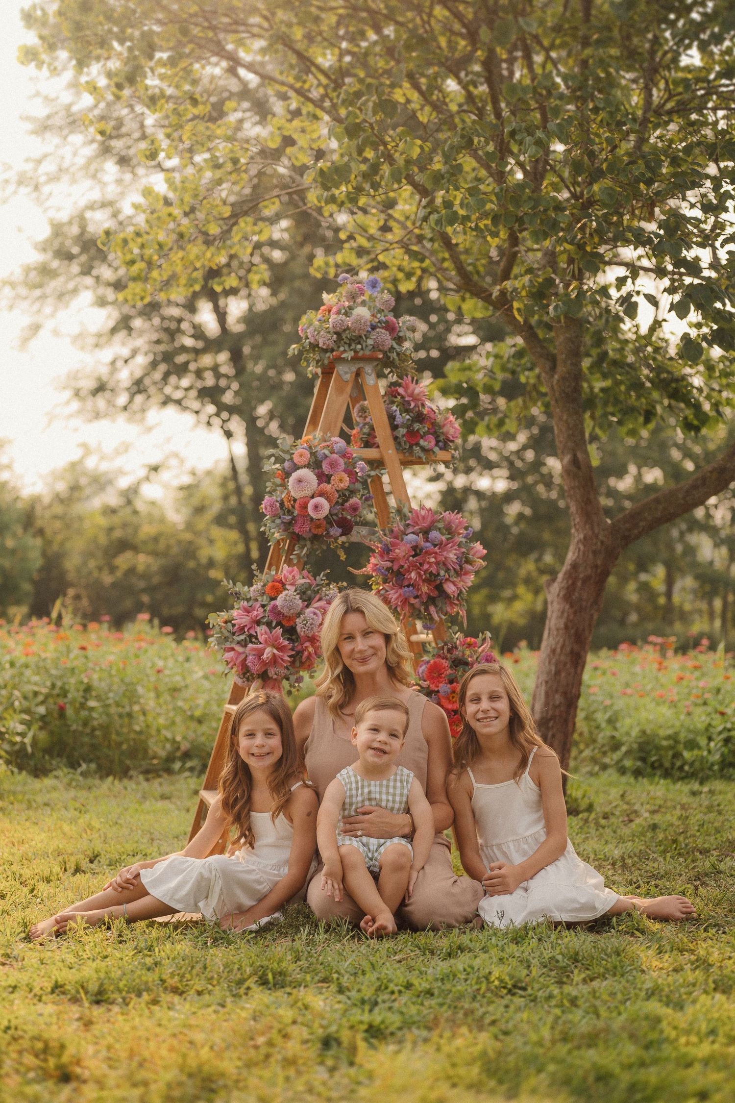 Outdoor portrait setting with wooden ladder decorated in pink and purple flowers under a leafy tree.
