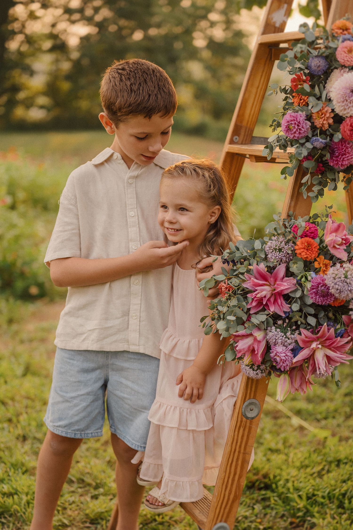 Rustic wooden step ladder decorated with pink and purple blooms stands in a sunlit grassy meadow.