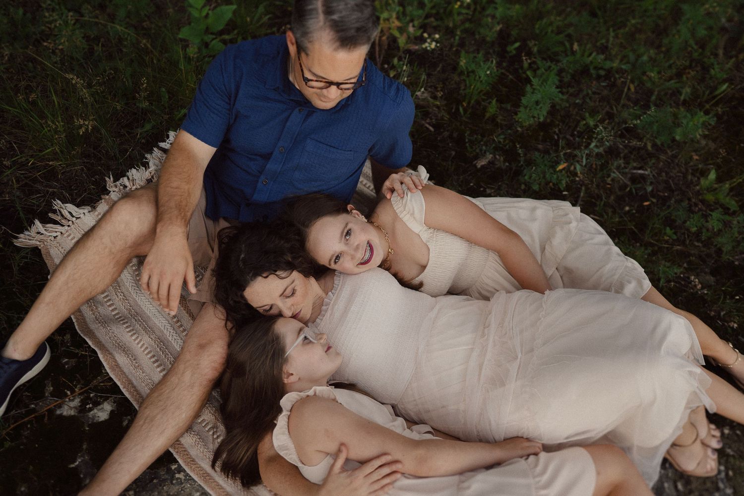 Intimate family portrait lying comfortably together in a natural outdoor setting on a blanket with pillows.