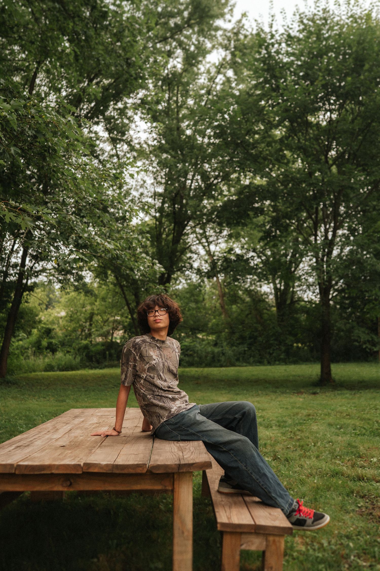 Someone relaxes on a rustic wooden picnic table in a peaceful outdoor setting surrounded by green trees.