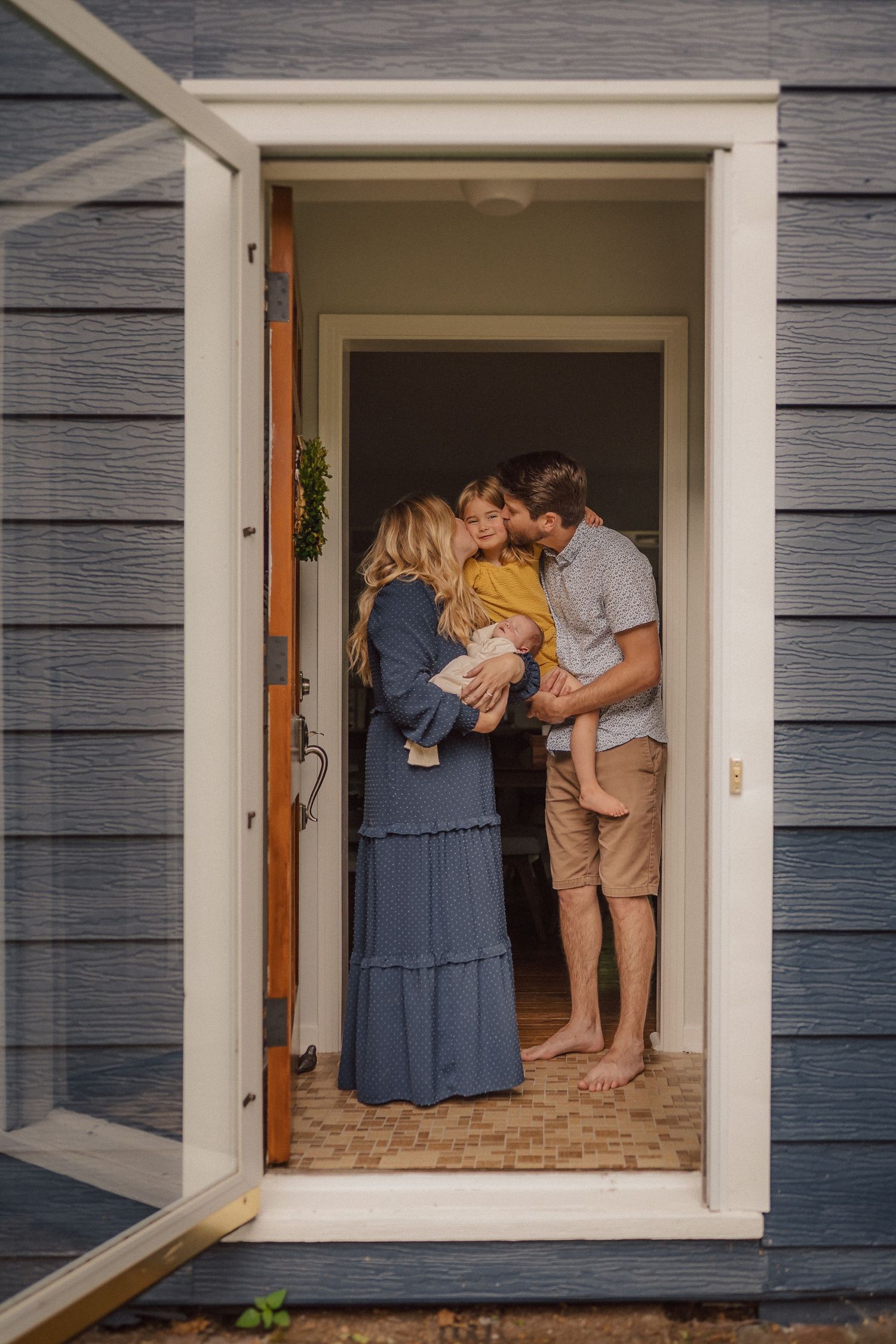 An intimate family gathering in a doorway of a blue-sided house.