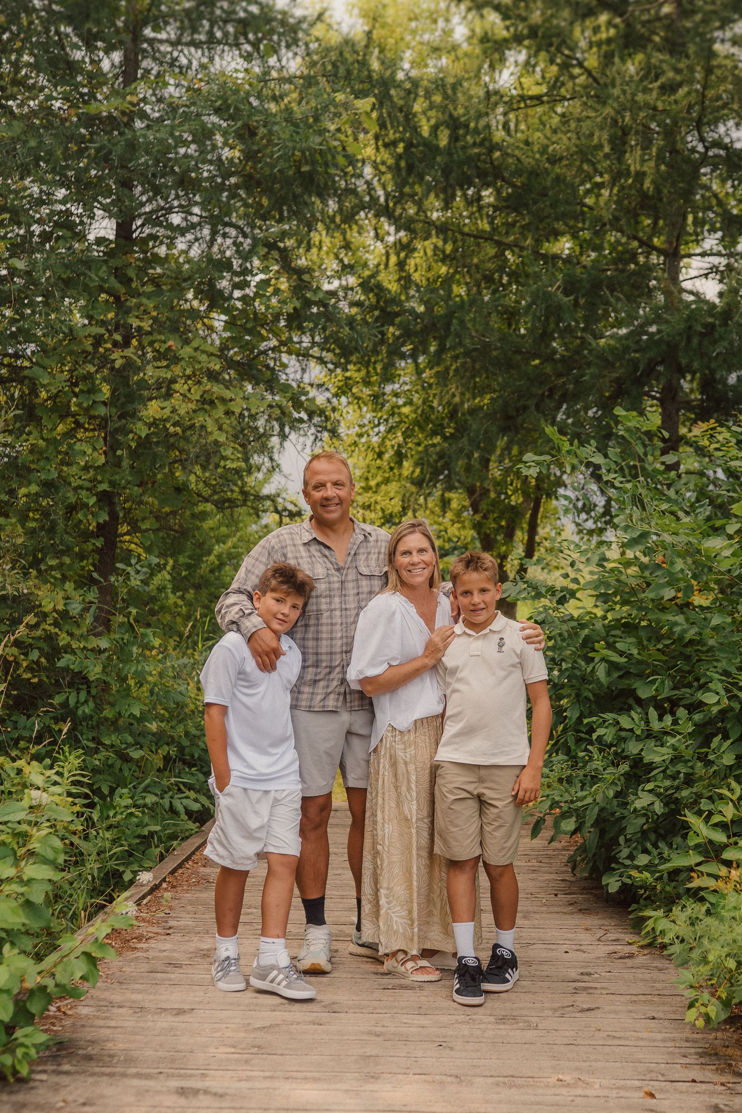 Group portrait of people in coordinated outfits standing on a wooden boardwalk amidst green trees.