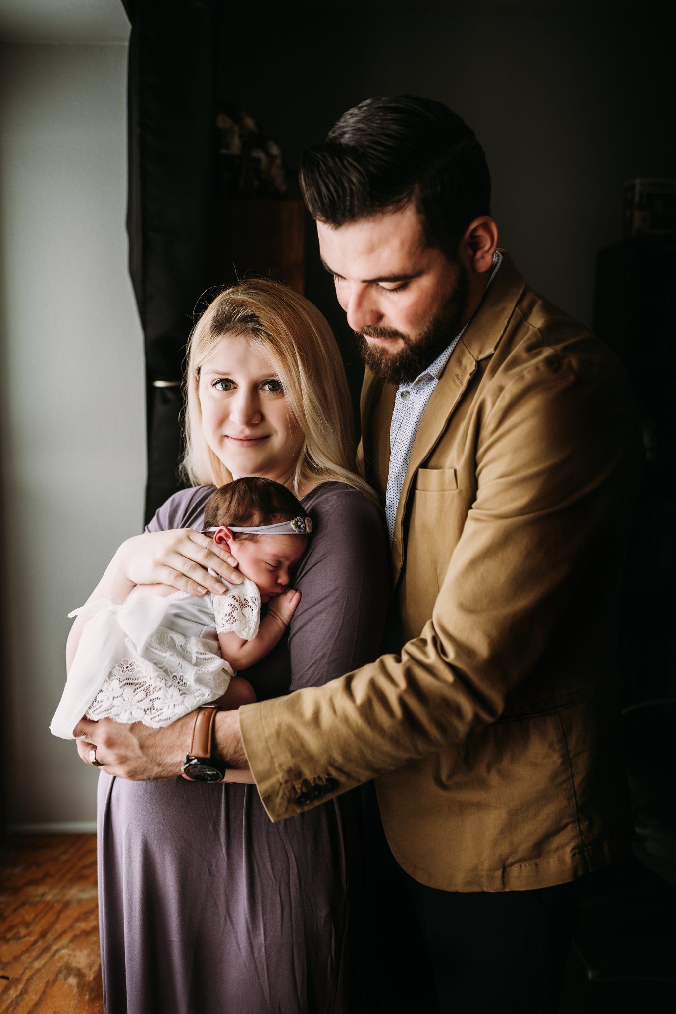 Family portrait with parents in casual attire holding newborn in white dress.