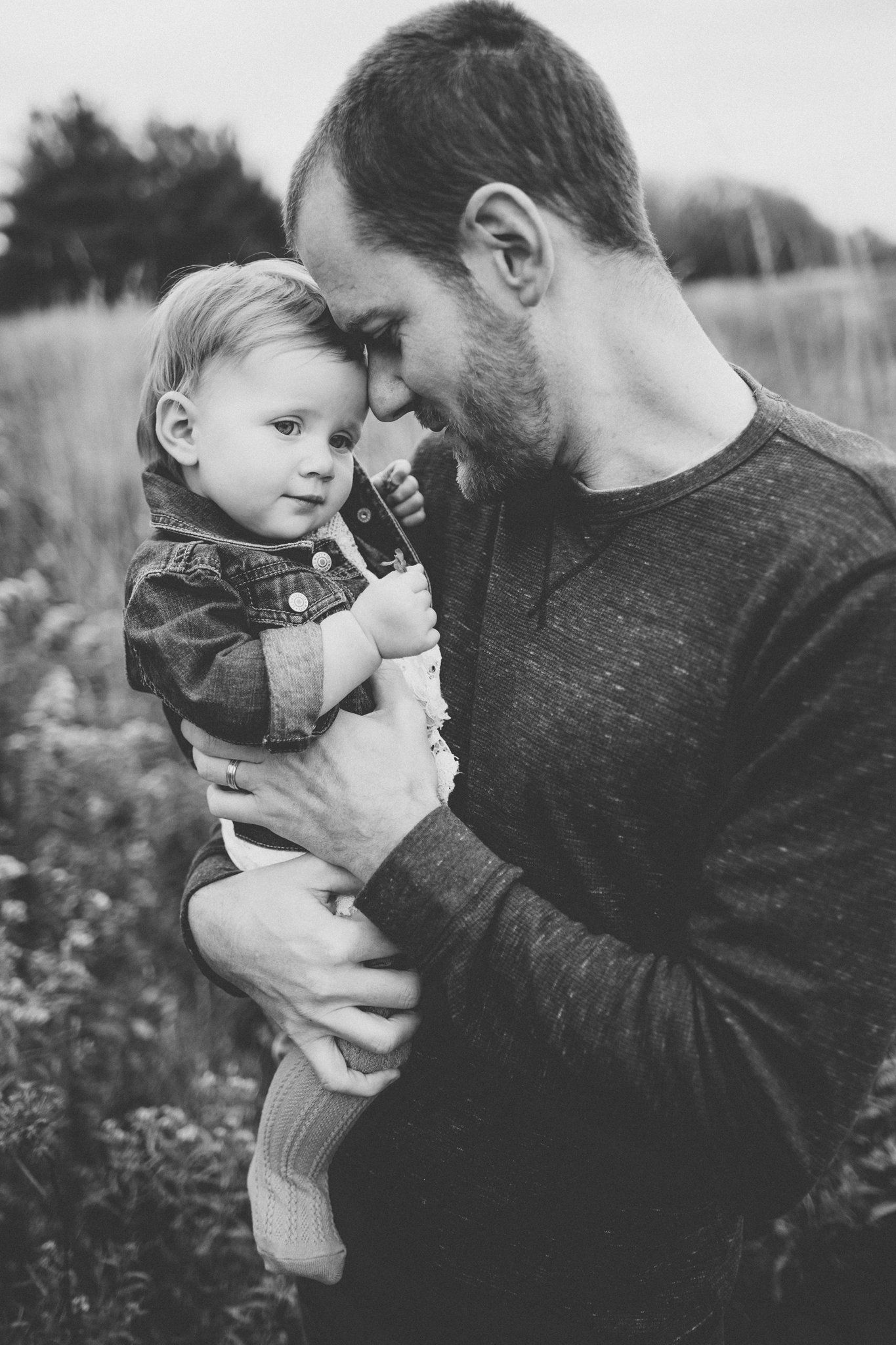 Black and white portrait of tender moment between parent and small child in outdoor field setting.