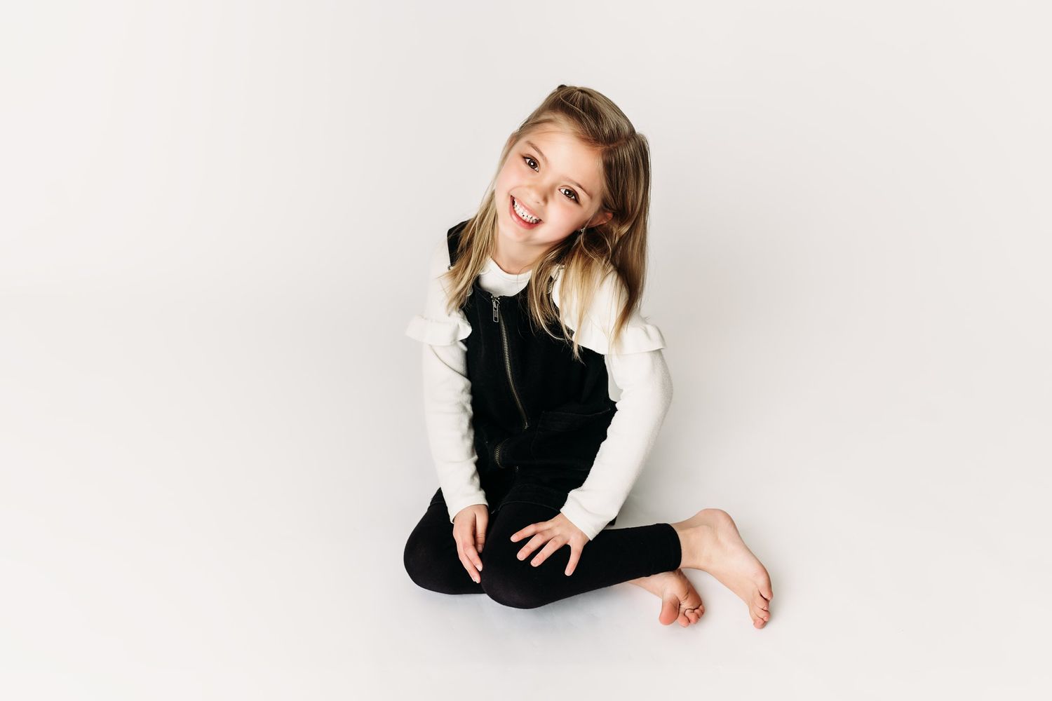A child sits cross-legged on white background wearing contrasting black and white outfit.