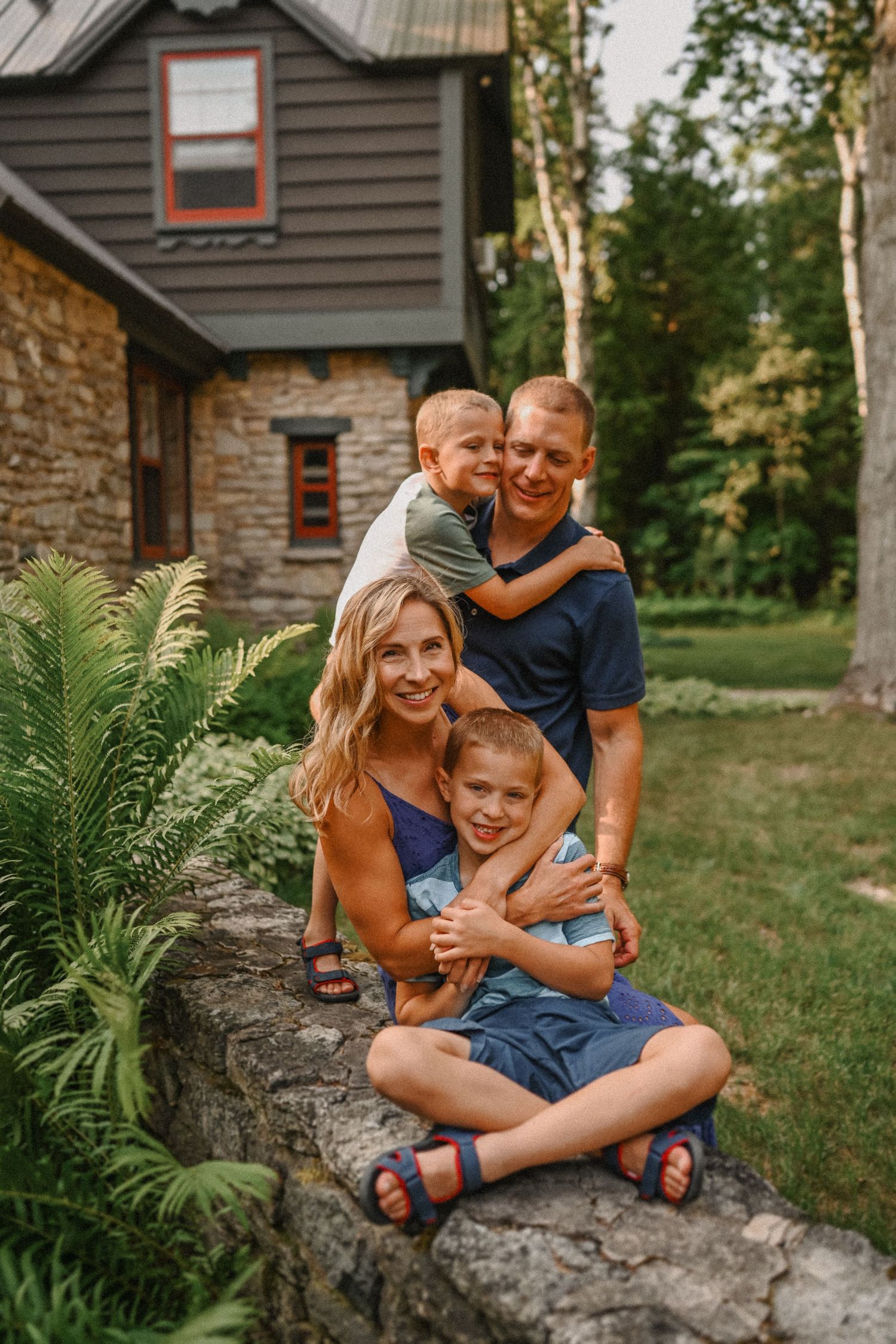 Family posing together on stone wall outside their cabin home.