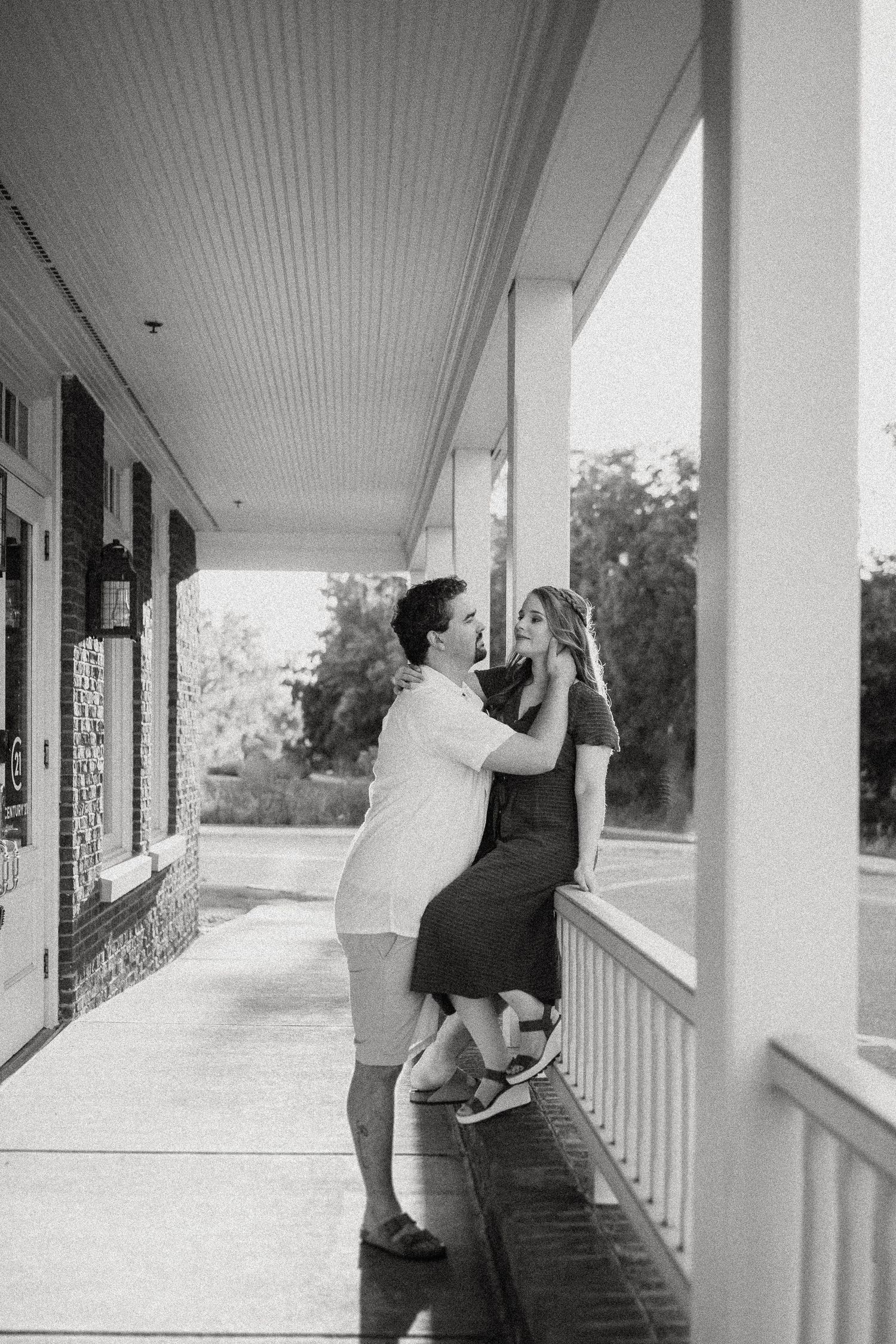 A romantic black and white photo of a couple embracing on a covered porch with white columns.