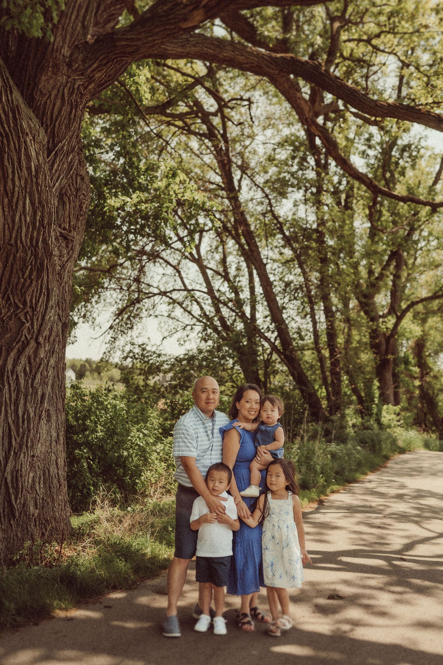Family posing for a photo on a sunlit path surrounded by towering trees.