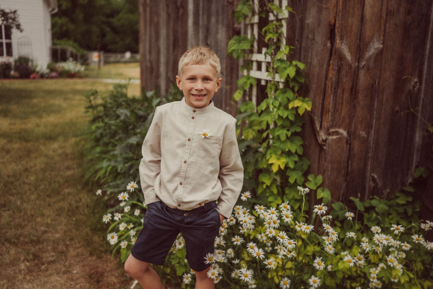 A child smiles while standing next to climbing vines and flowers in a summer garden setting.