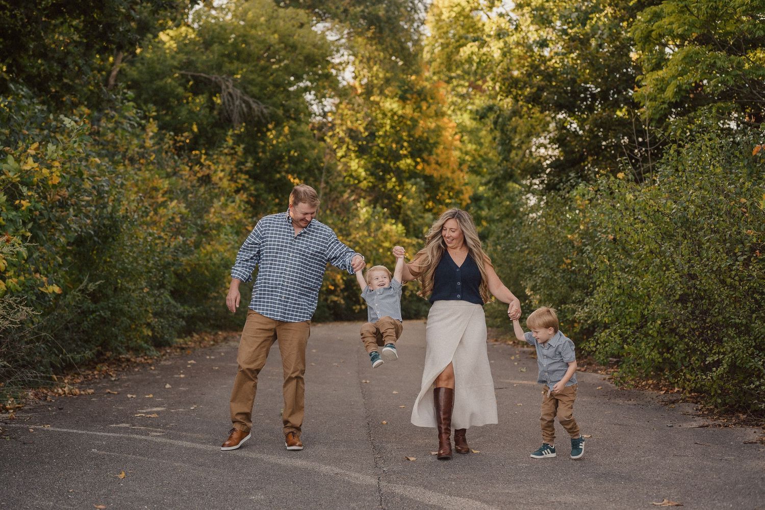 Family walking together on a wooded path during golden hour with autumn foliage in the background.