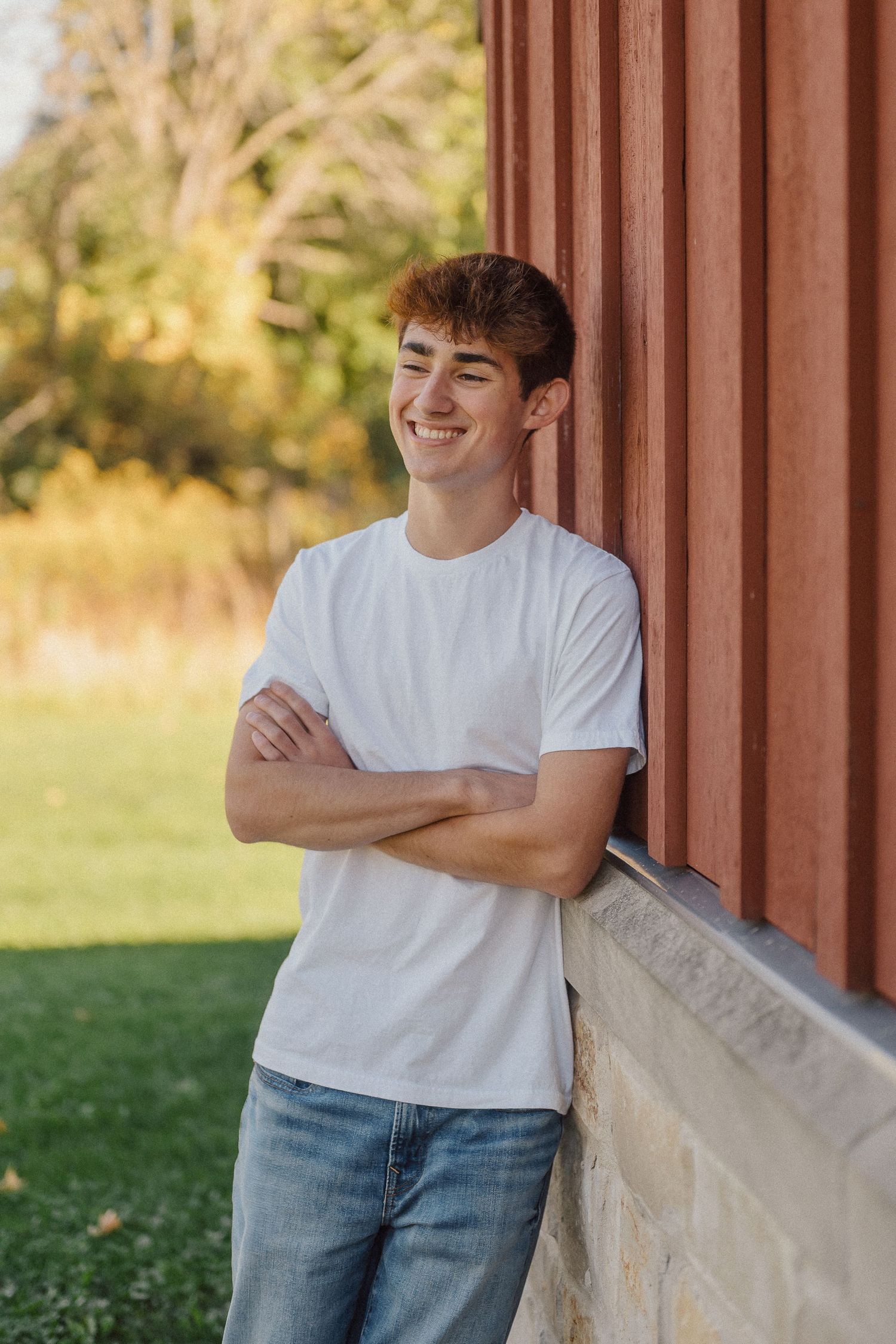 Person in white t-shirt and jeans leaning against a rustic brown wall in warm autumn light.