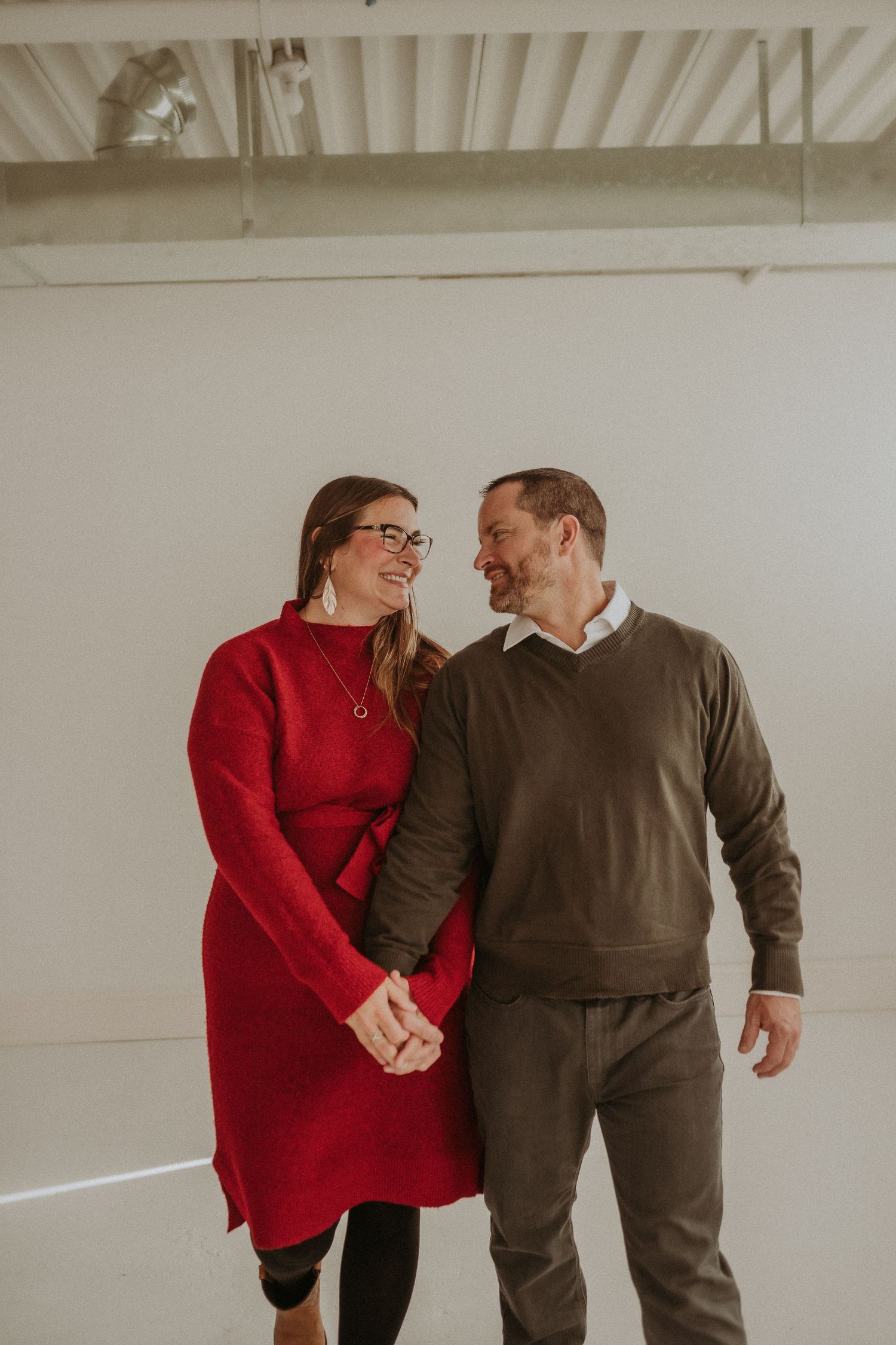 A couple shares a tender moment in a studio, wearing coordinating red and brown sweaters.