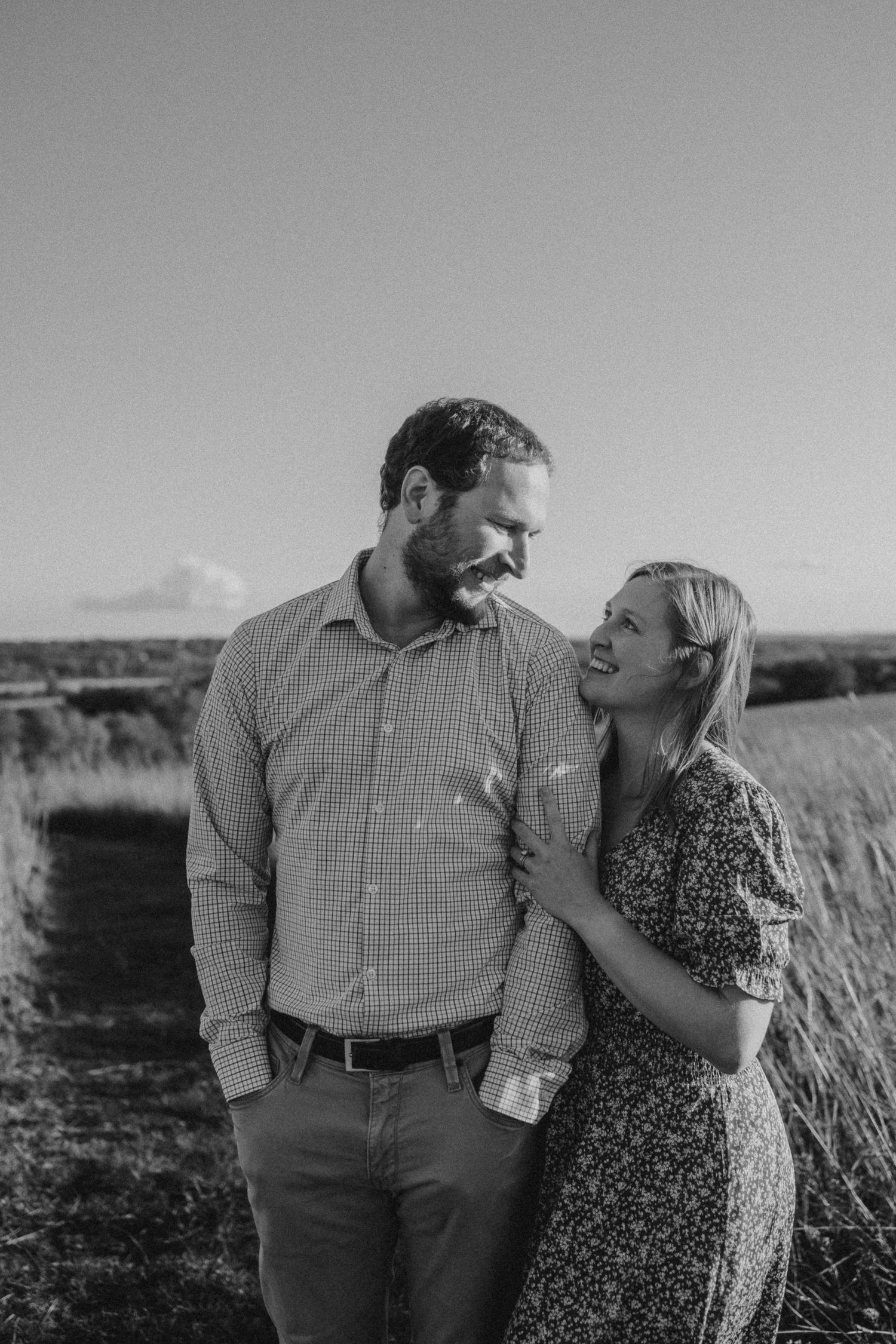 Black and white portrait of a couple sharing a joyful moment in an open field.