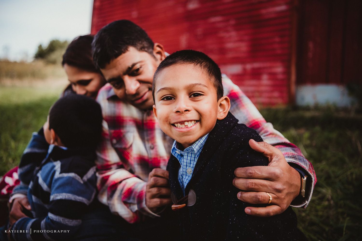 Candid family moment captured during outdoor photo session by red barn.