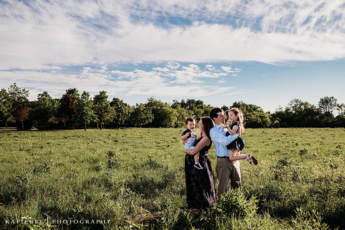 Family enjoying playful moments together in a green field under cloudy summer skies.