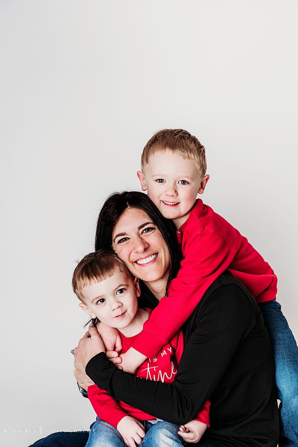 Heartwarming family portrait with coordinated red and black outfits against white backdrop.