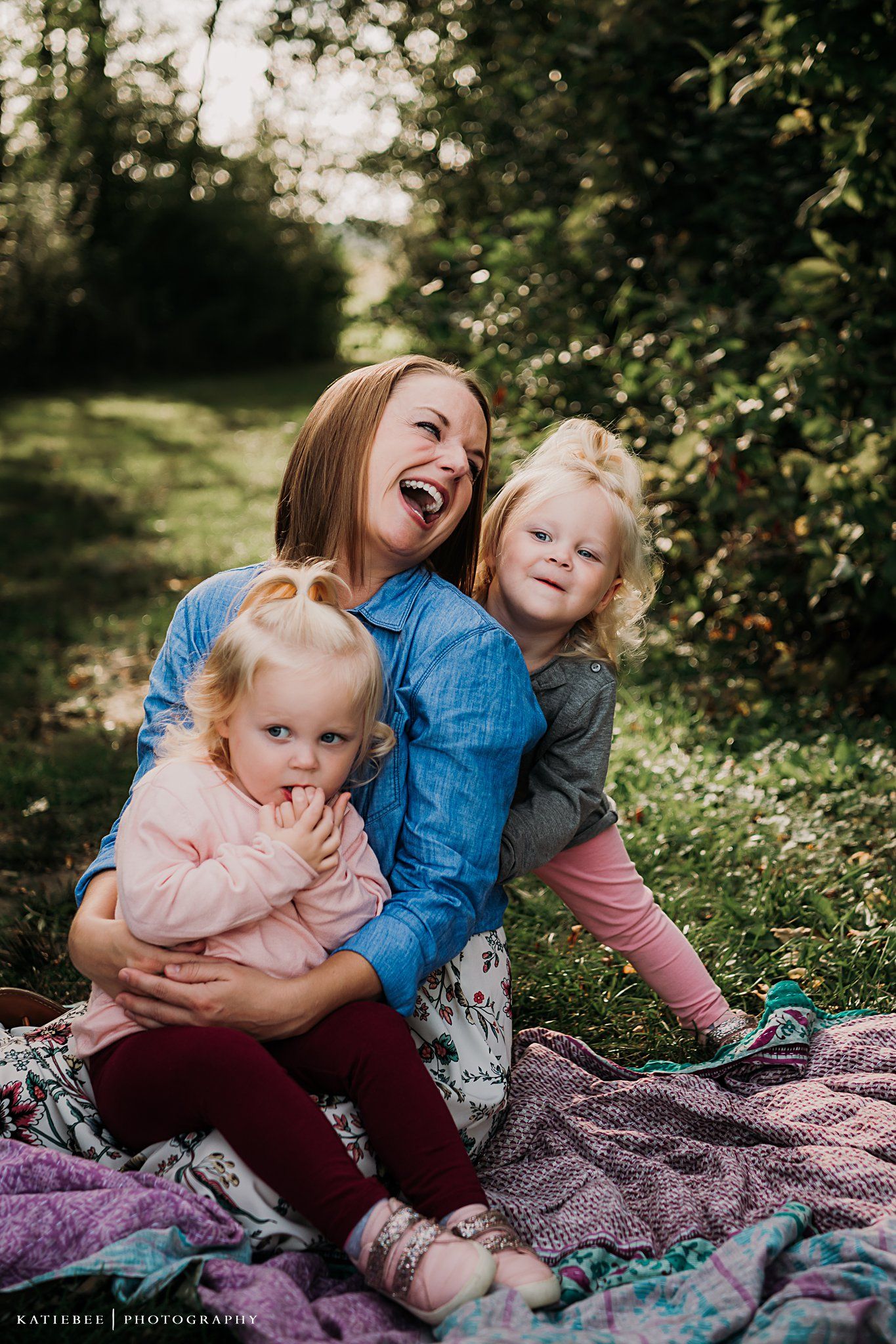 A joyful outdoor family moment captured on a blanket in dappled sunlight.