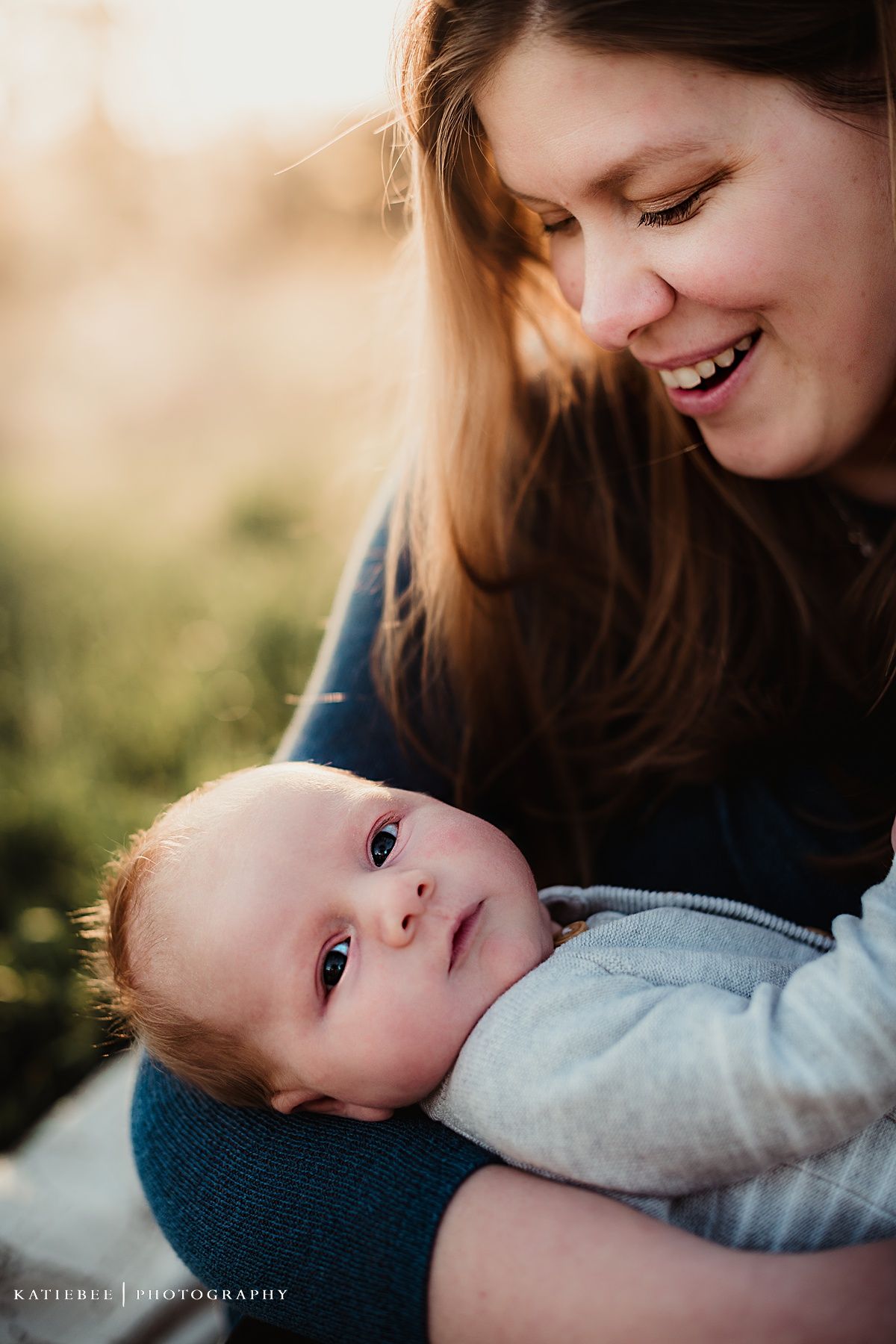 Close-up portrait capturing a joyful interaction between parent and baby against blurred nature background.