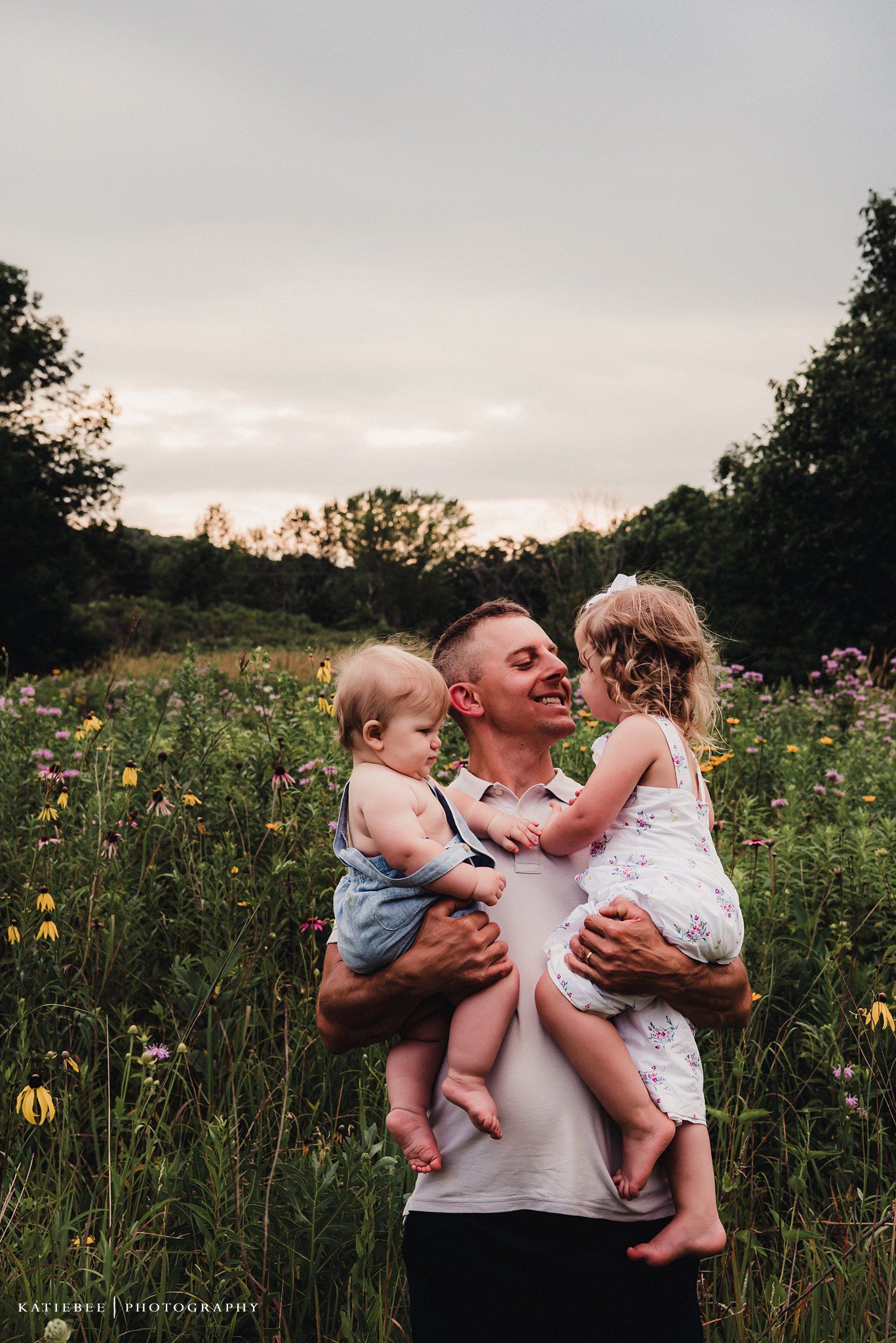 Happy family moment in a wildflower field during sunset as parent holds two young children.