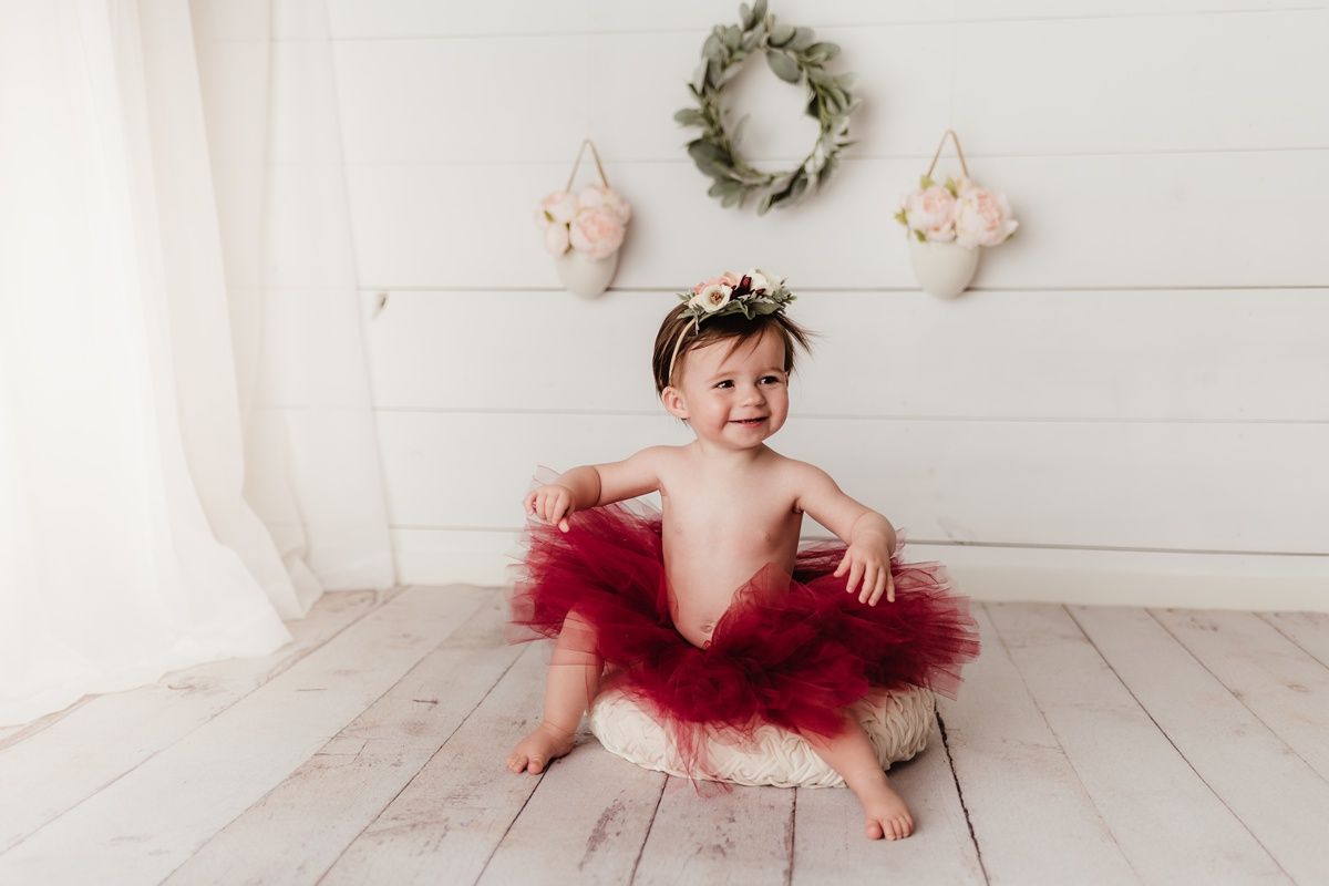 Birthday photo setup with burgundy tutu and rustic wall decorations including wreath and stars.