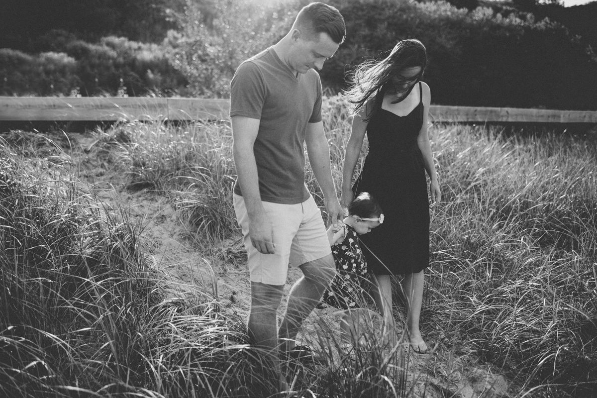A couple strolls together through tall grass in a dreamy black and white photo at sunset.