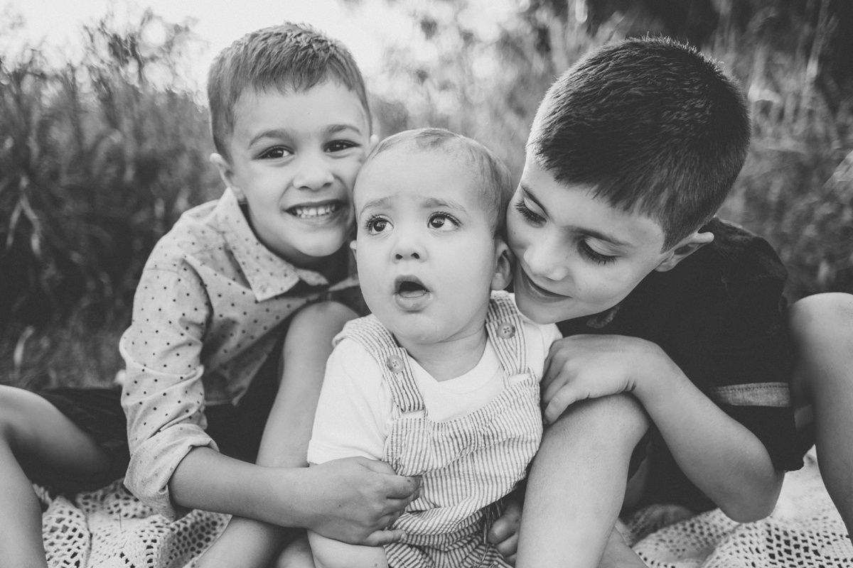 Black and white candid photo of three siblings embracing outdoors.