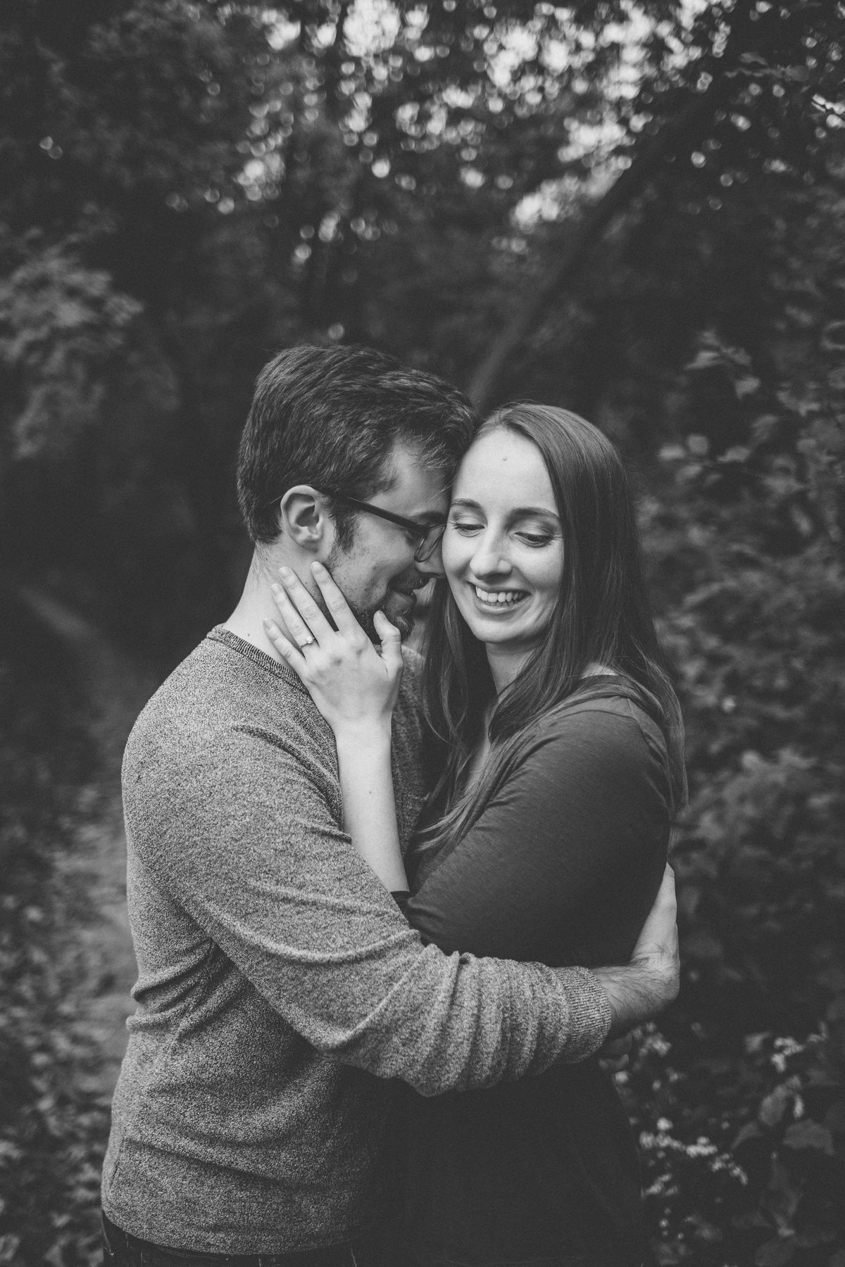 Intimate black and white portrait of couple embracing and laughing in natural setting.