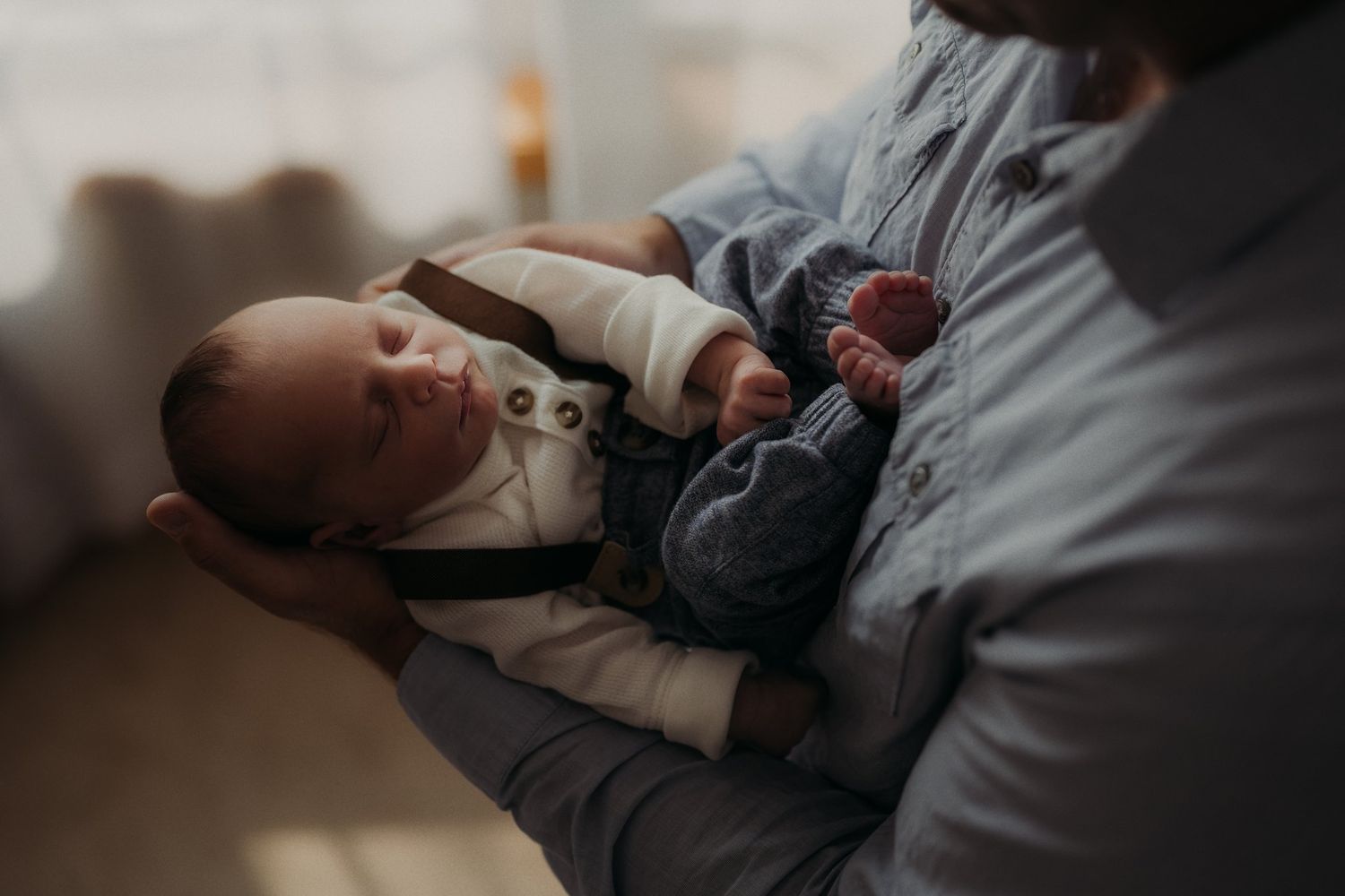 Newborn baby wearing white onesie rests peacefully in parent's arms.