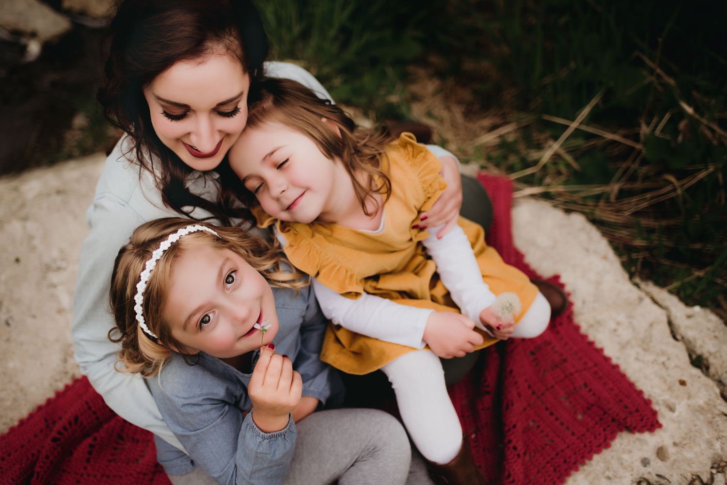 Candid family moment on a red blanket showing playful affection and laughter outdoors.