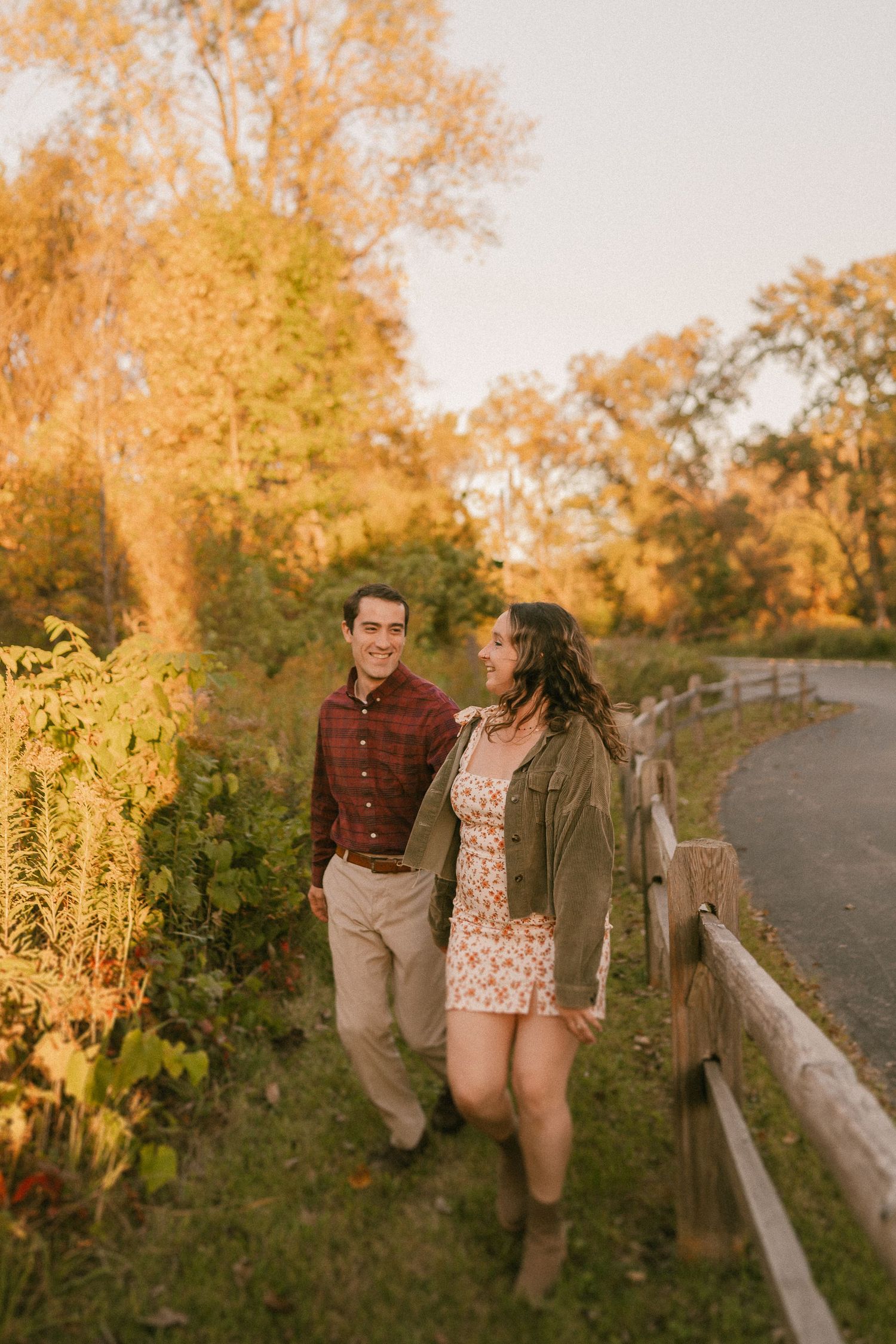 Couple walking along rustic fence path during autumn sunset.