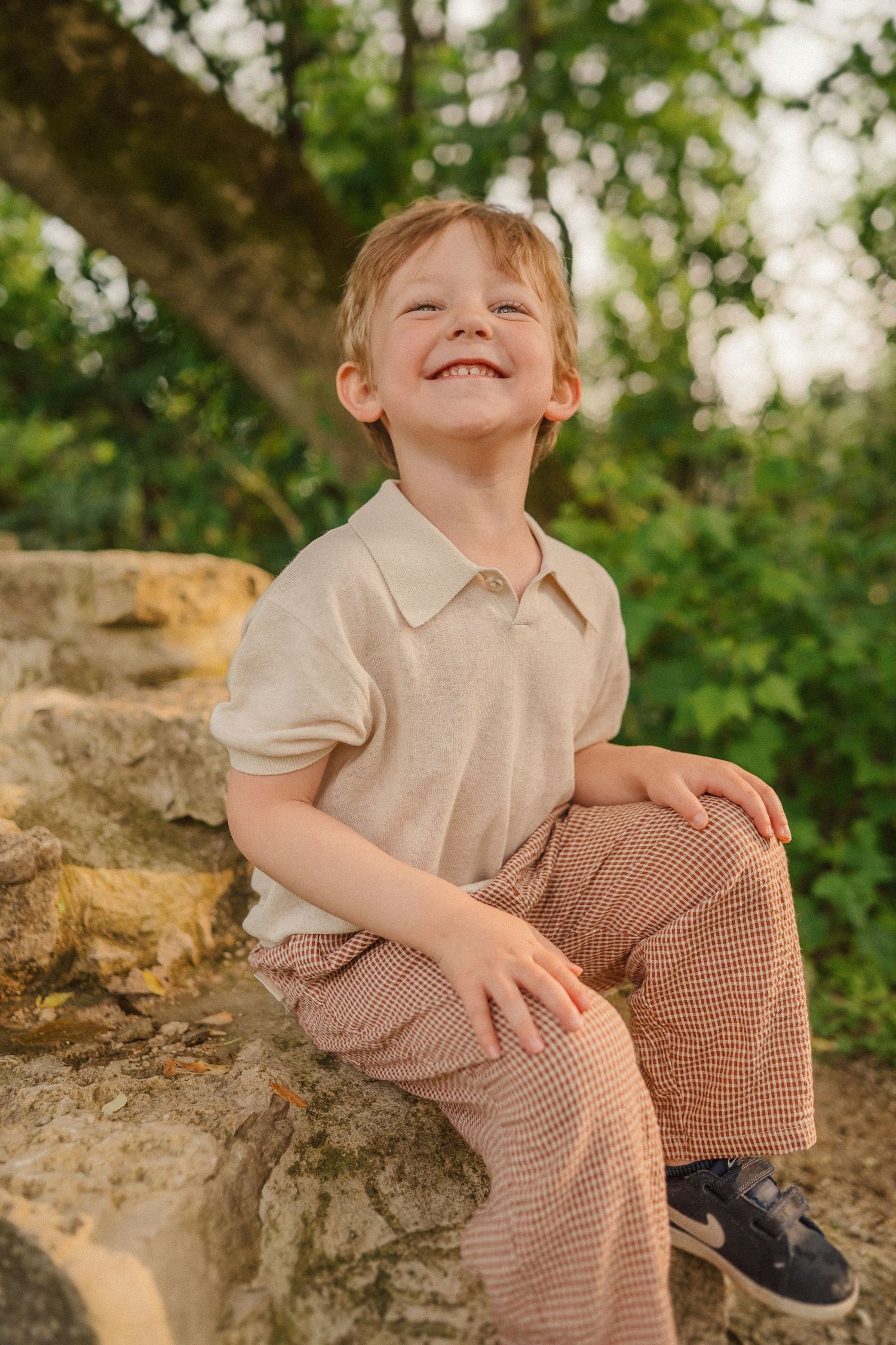 A joyful moment captured outdoors of someone sitting on stone steps wearing a beige polo and patterned pants.