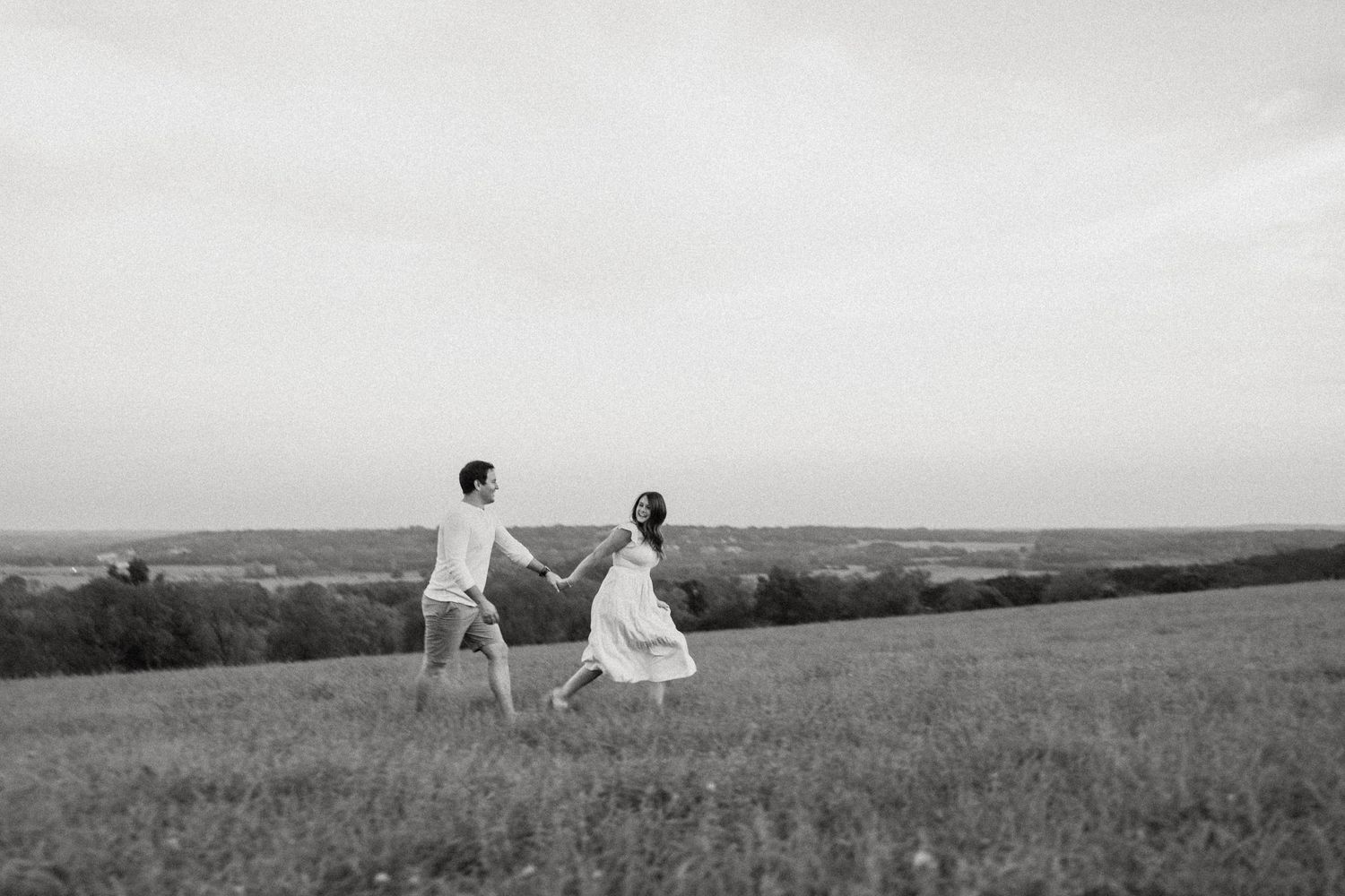 Black and white photograph of two people walking hand in hand across a hilltop meadow.