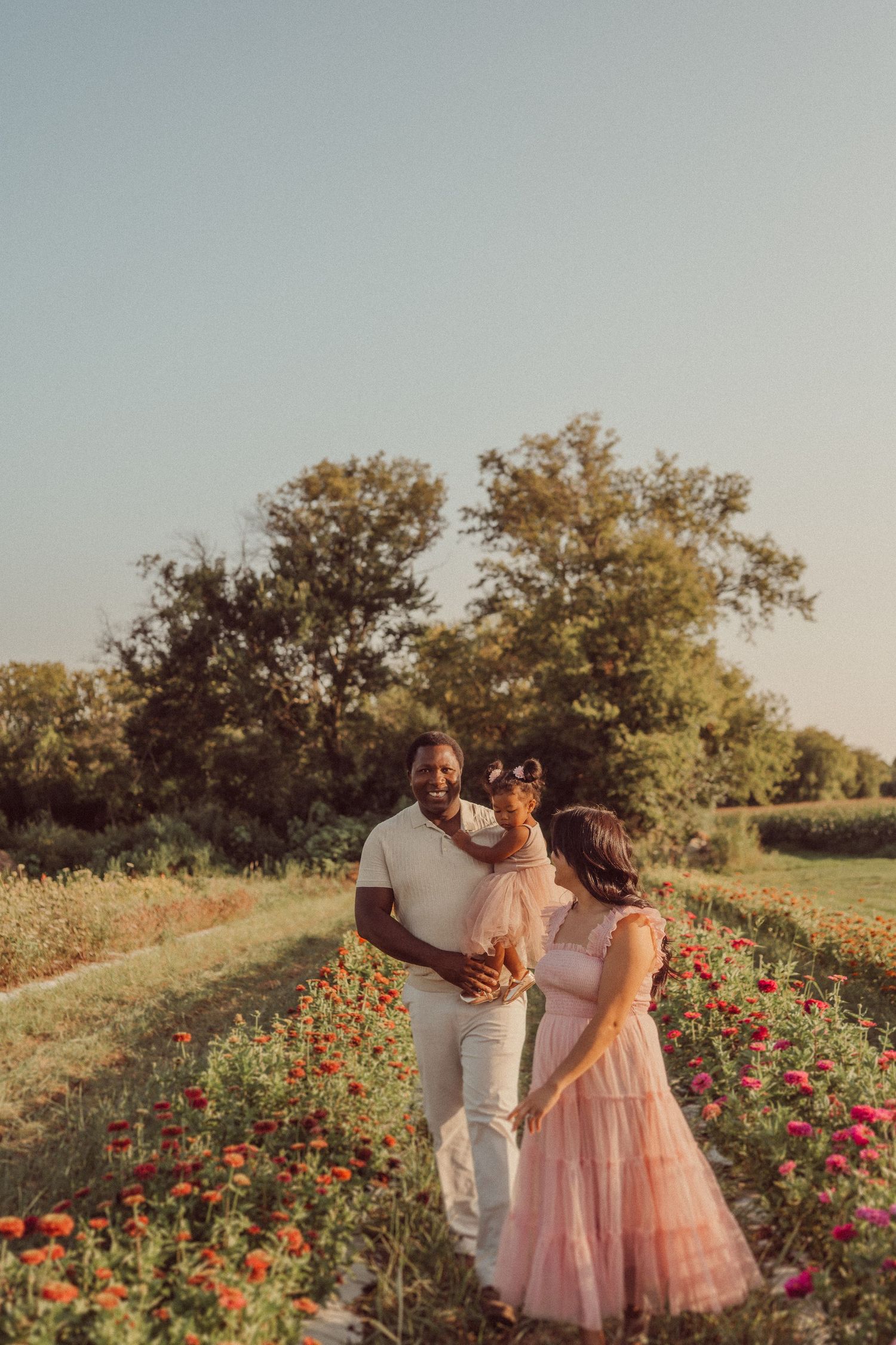 A family standing together in a flower garden path during sunset.