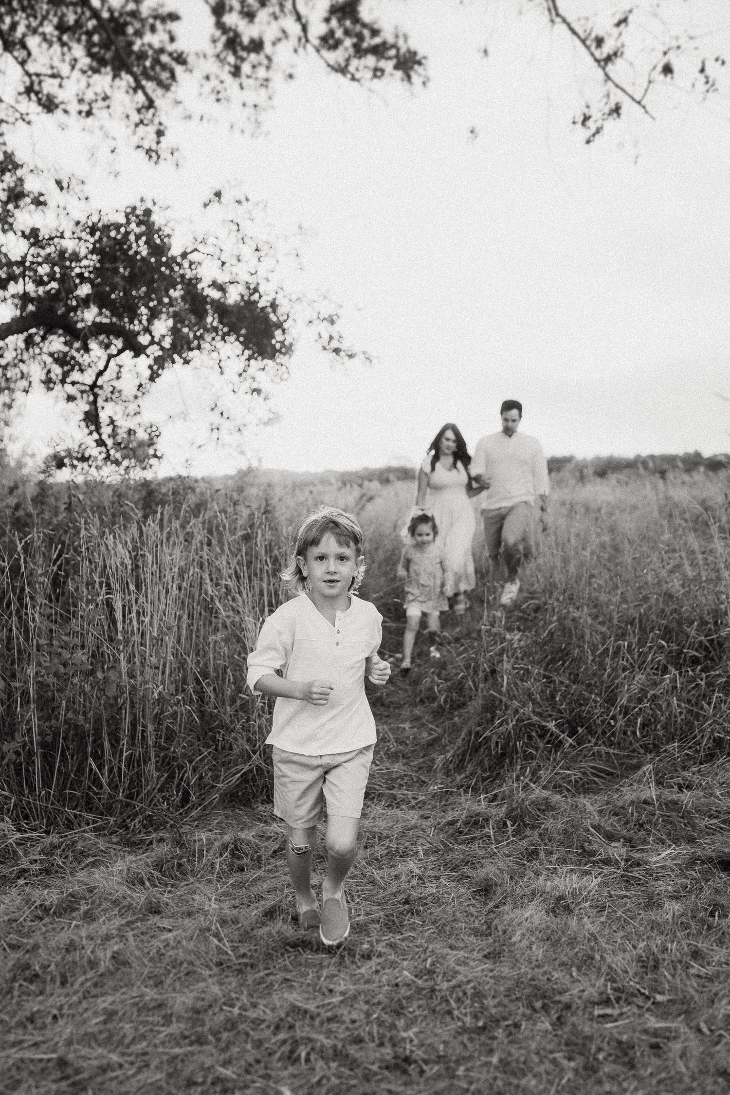 A family walks together through a grassy field with trees in the background in black and white.