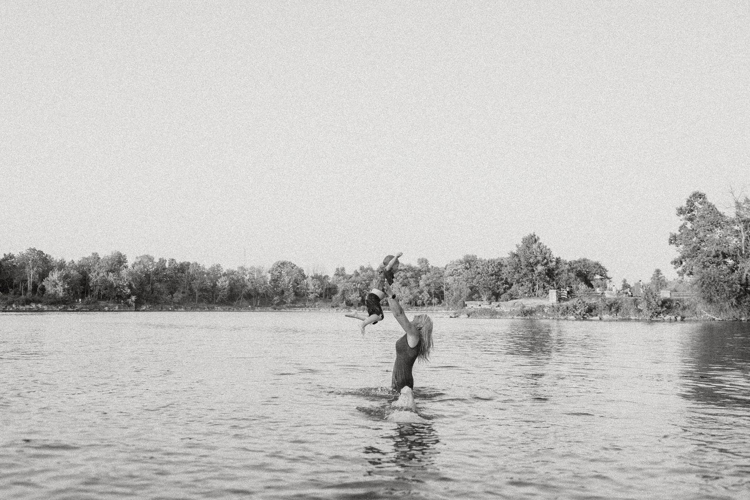 Black and white photo of people playing and splashing in a tranquil lake.