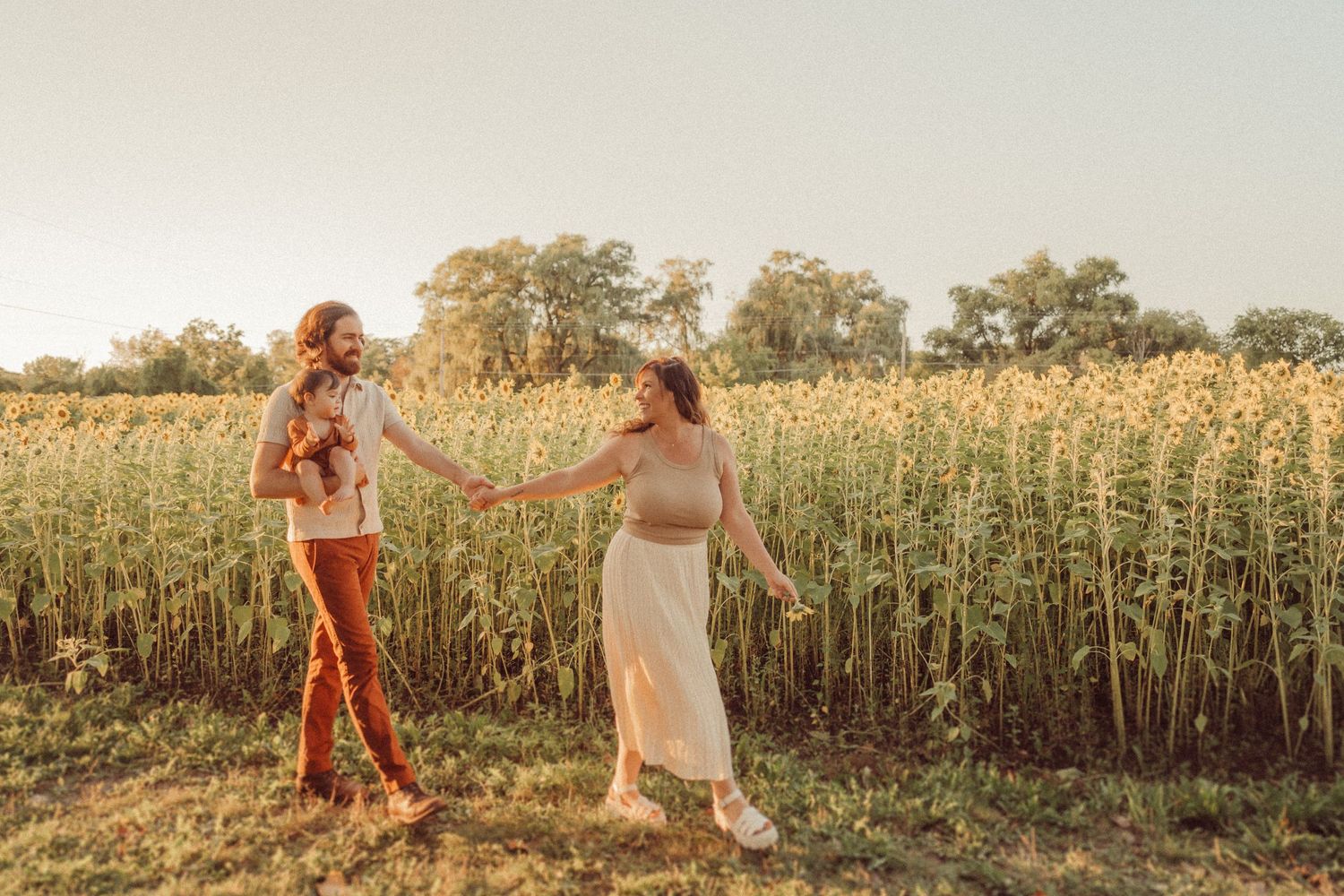 Two people share a playful moment beside a sunflower field at sunset.